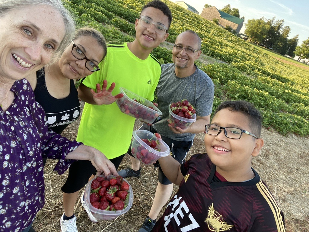 A selfie photo of five people holding baskets of strawberries in a field.