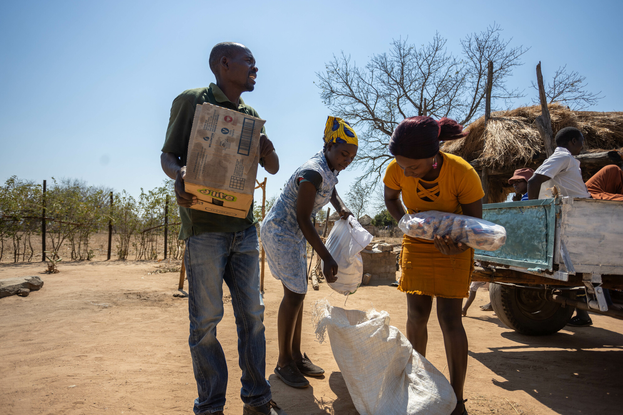 Three people unload food from the back of a truck.