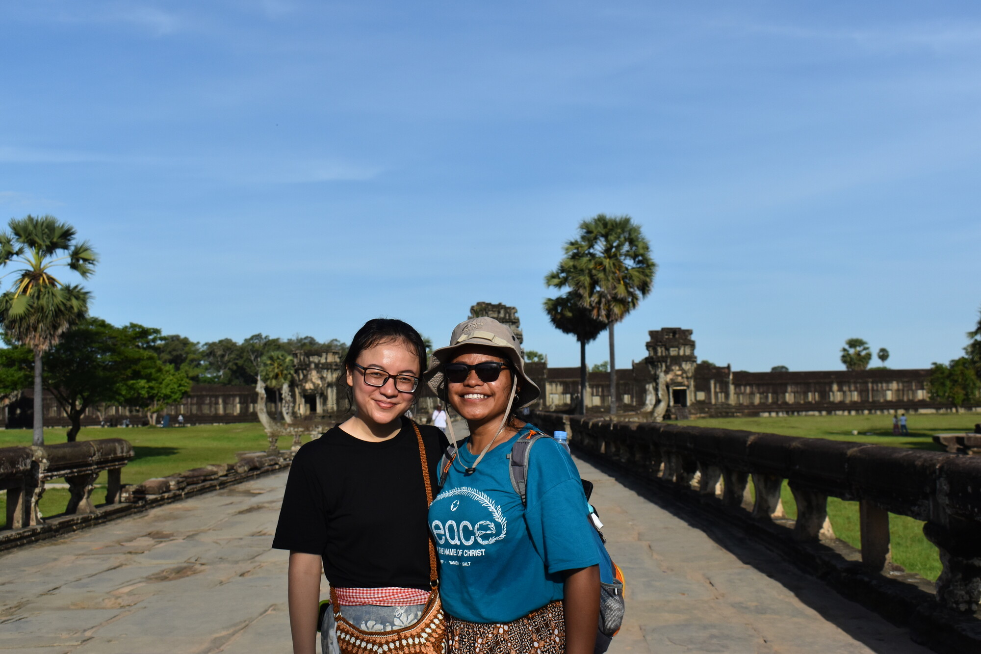 Two women standing side by side on a path with Angkor Wat in the background