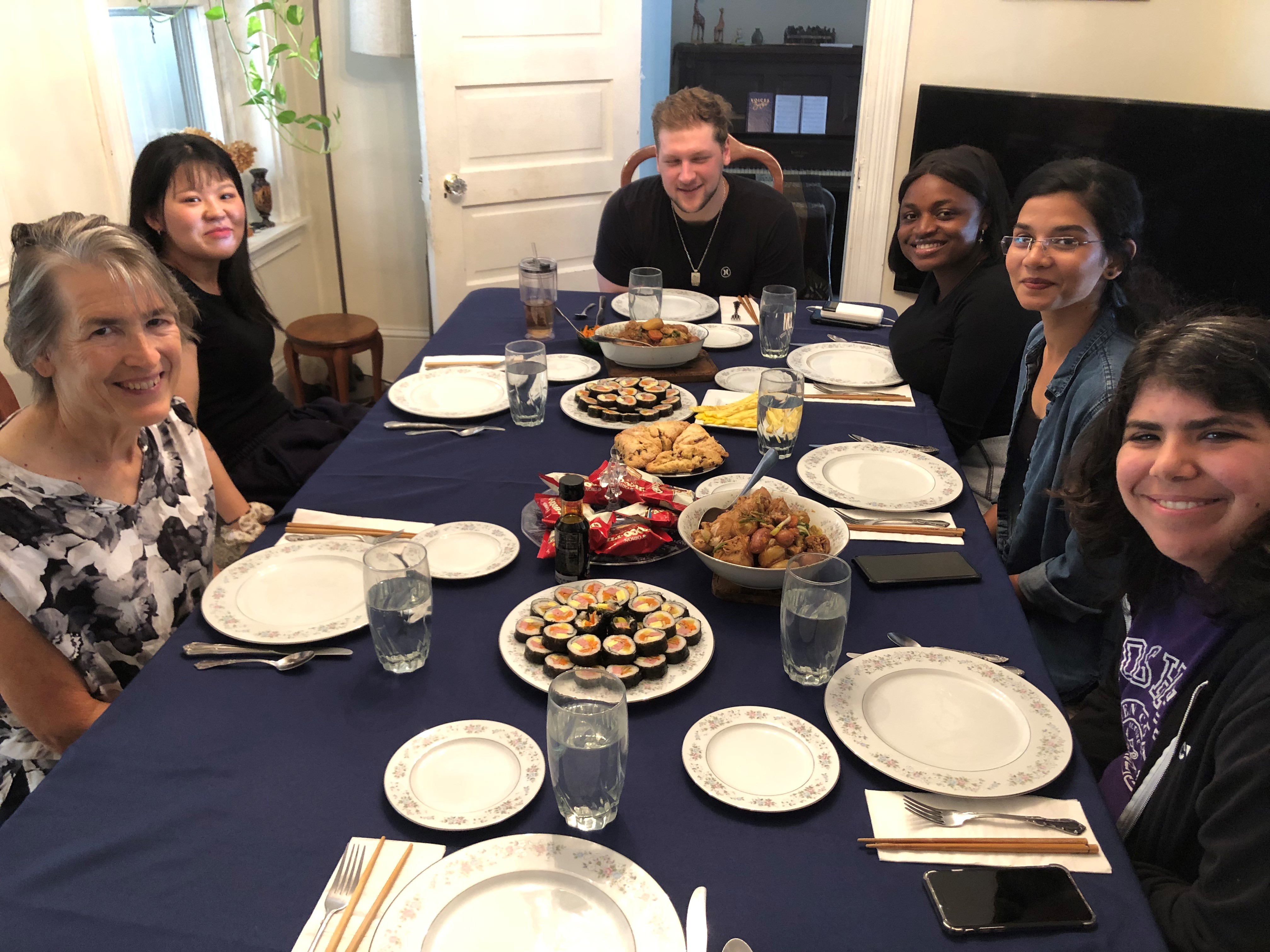 Six people sit around a table set with various plates of Korean food.