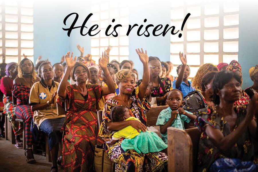 People in a church with hands raised and the words "He is risen!"