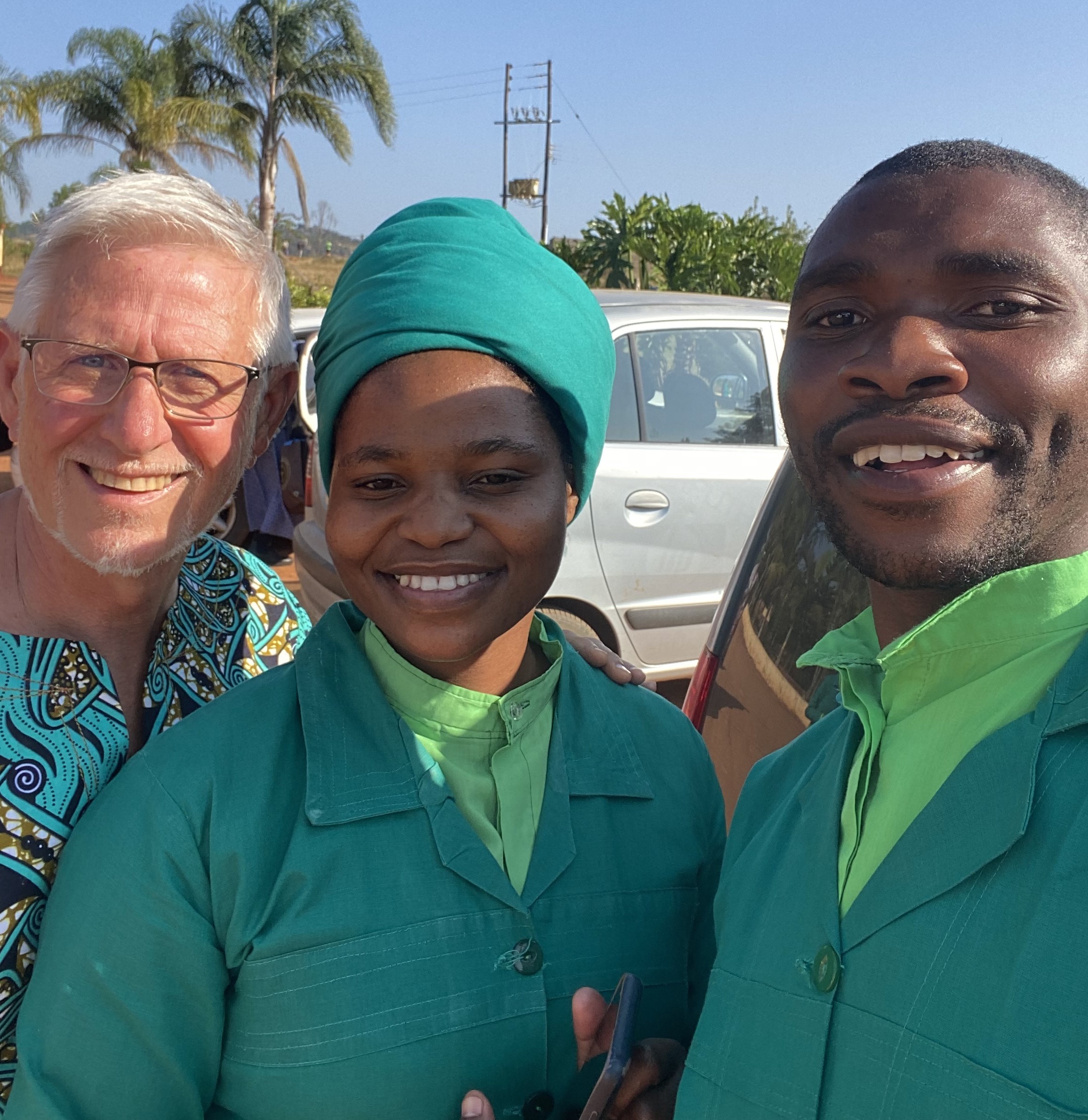 Three people in green church clothes stand together smiling at the camera.