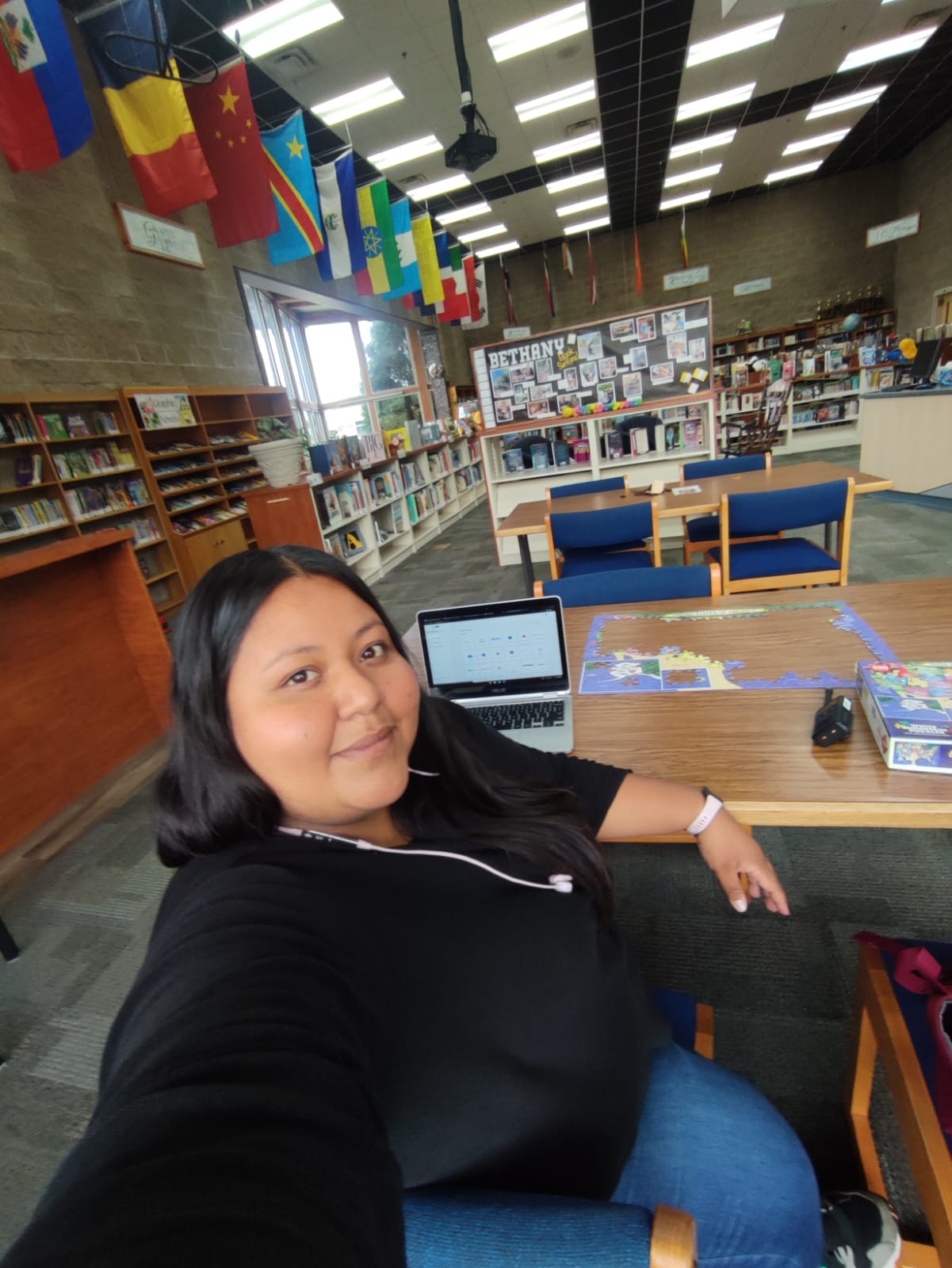 A young adult sits in a chair in a library with flags from several different countries hanging from the ceiling.