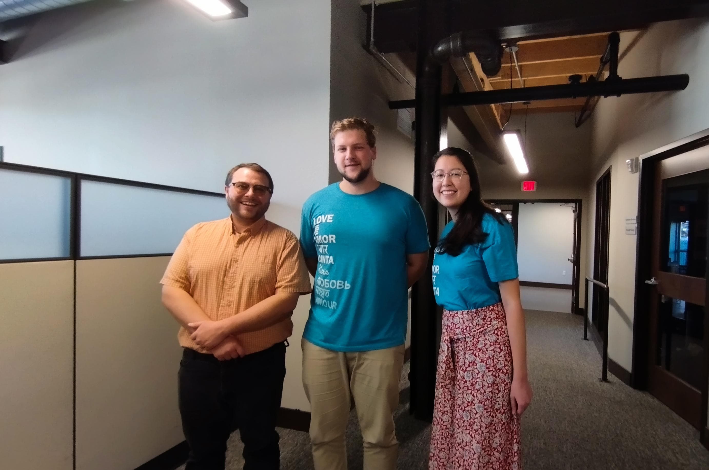 Three people stand together in the hallway of a building.