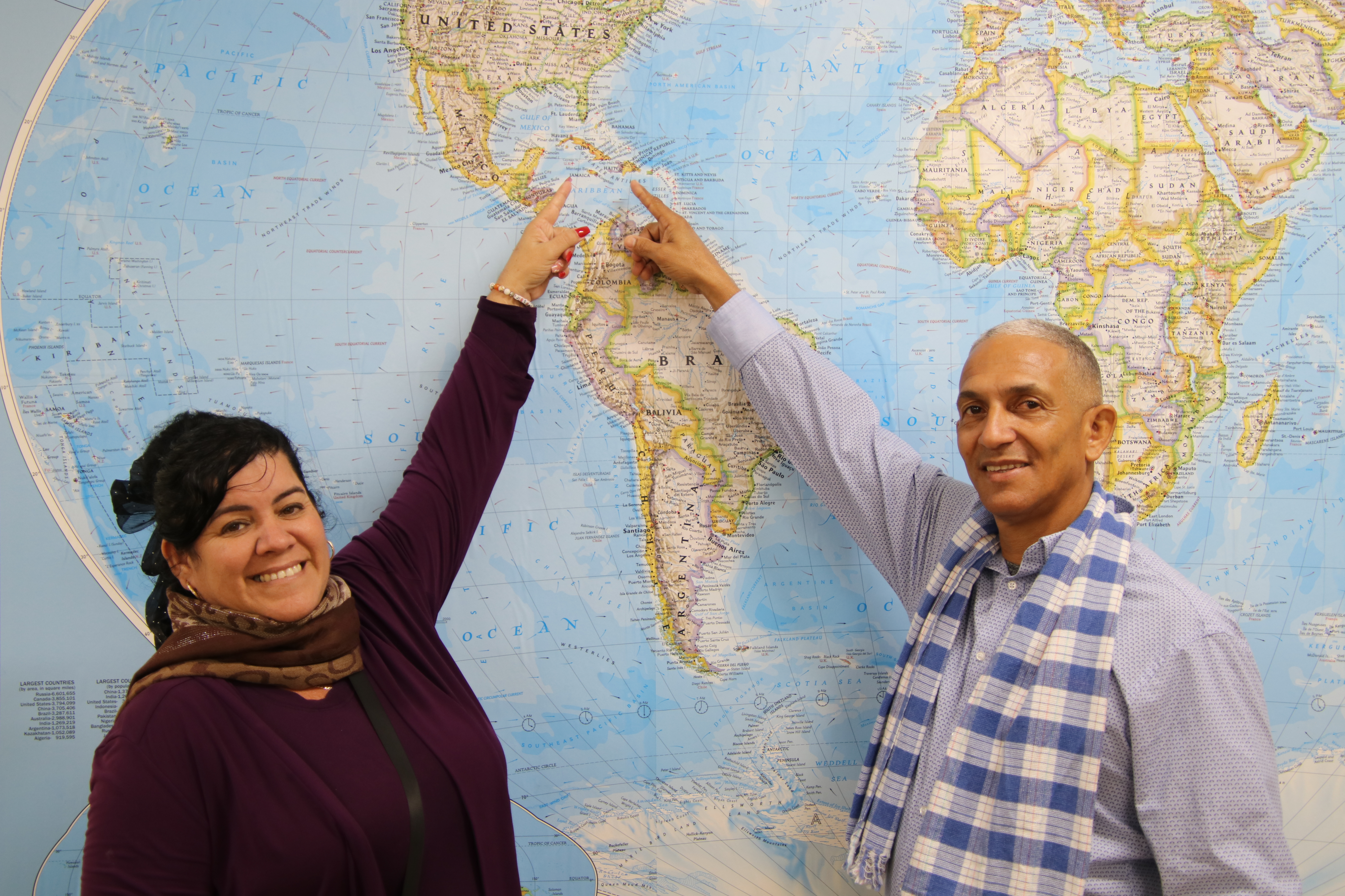 A man and woman together point to Cuba on a map