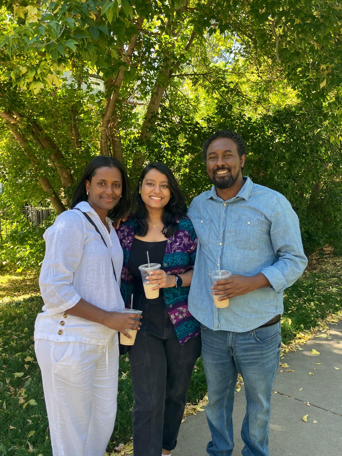 A young adult and her host parents stand in front of a tree holding plastic cups.