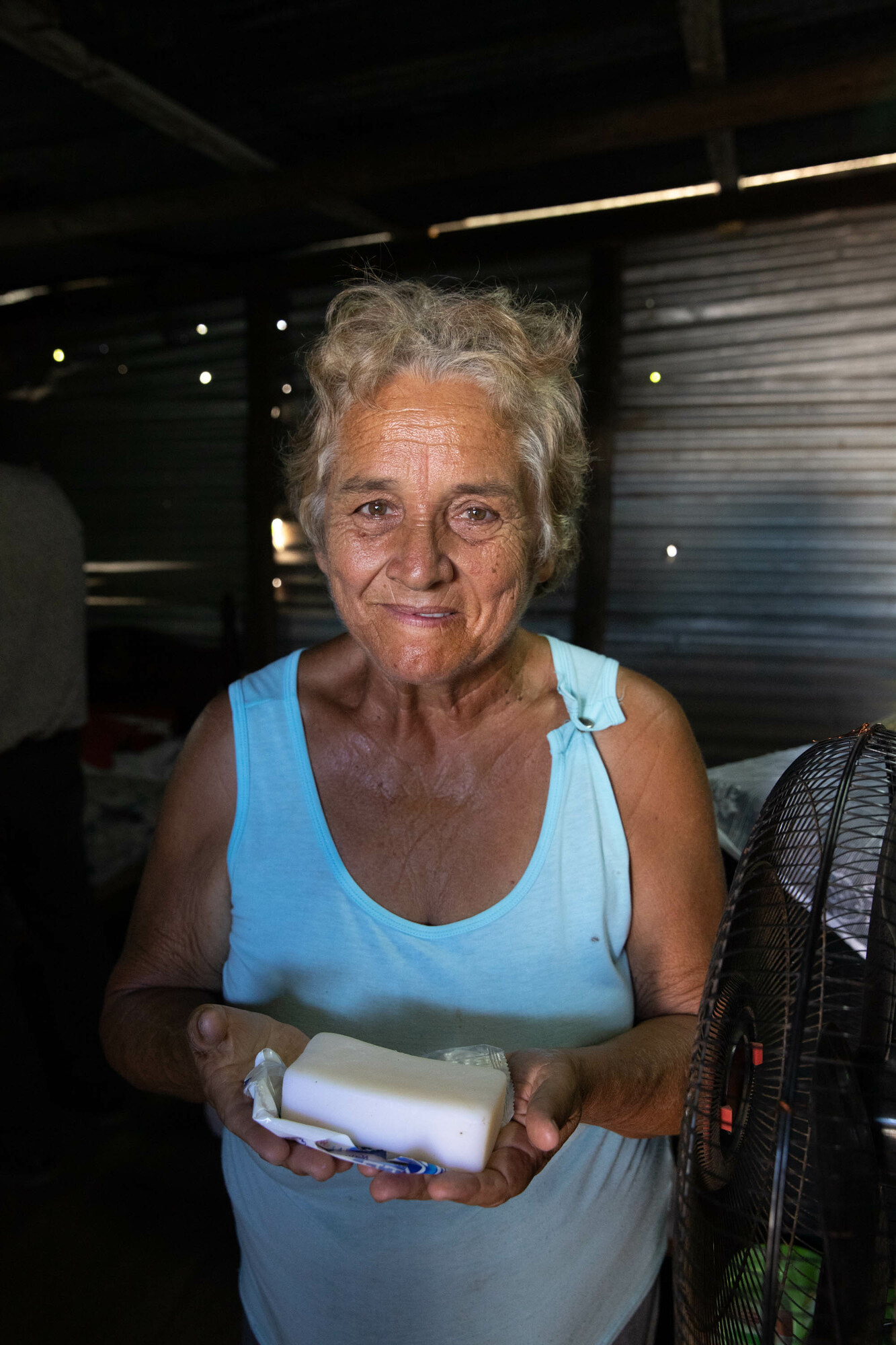 White-haired woman in blue tank top holding bar of soap inside a building