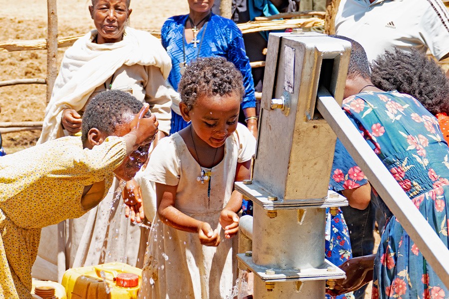 A group of children drinking from a well.