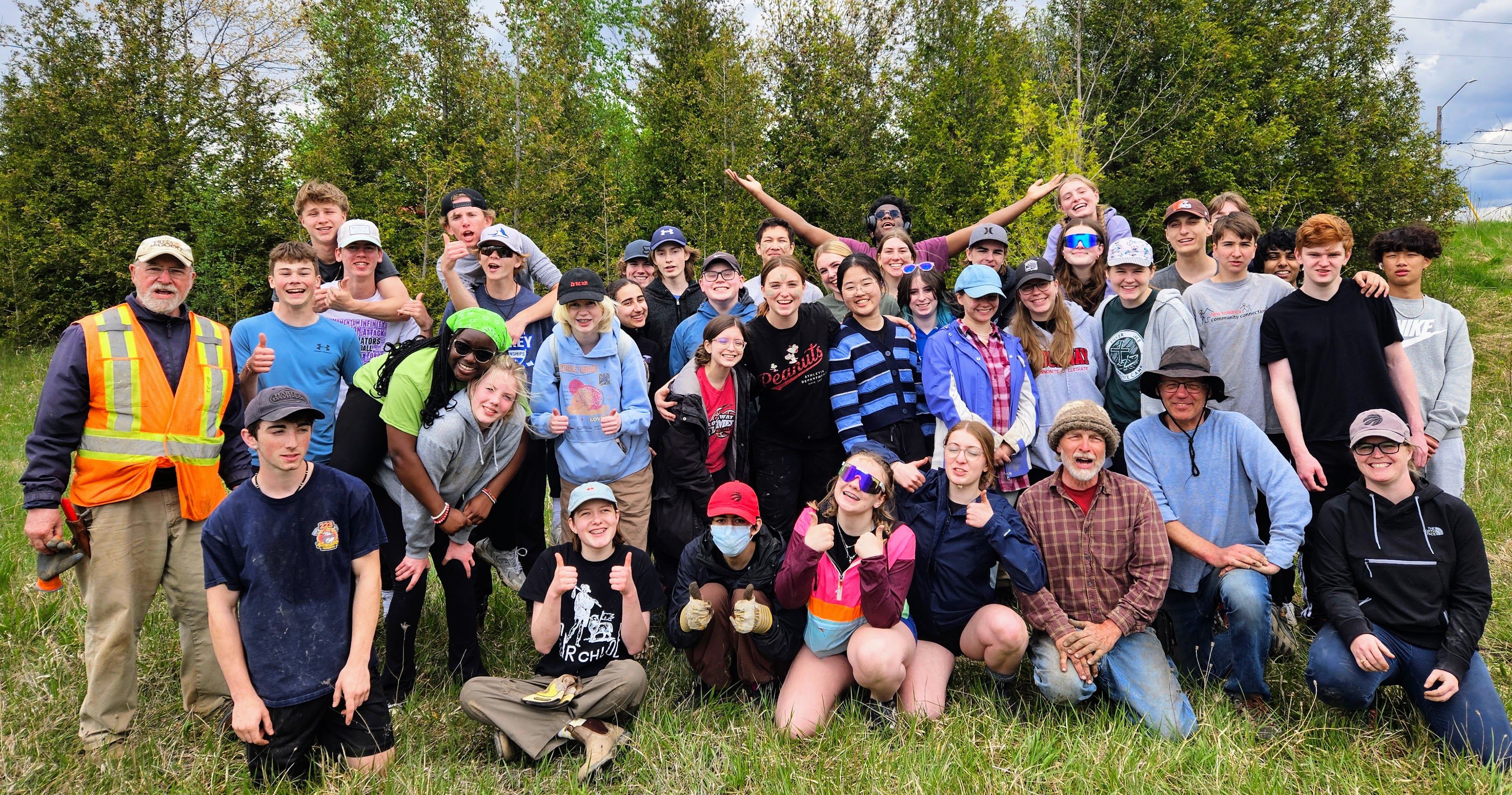 A group of several youth and four adults post for the camera in a green field.