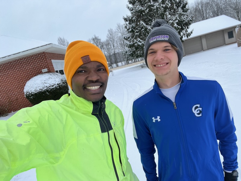 Two people stand in the snow wearing warm hats and running apparel.