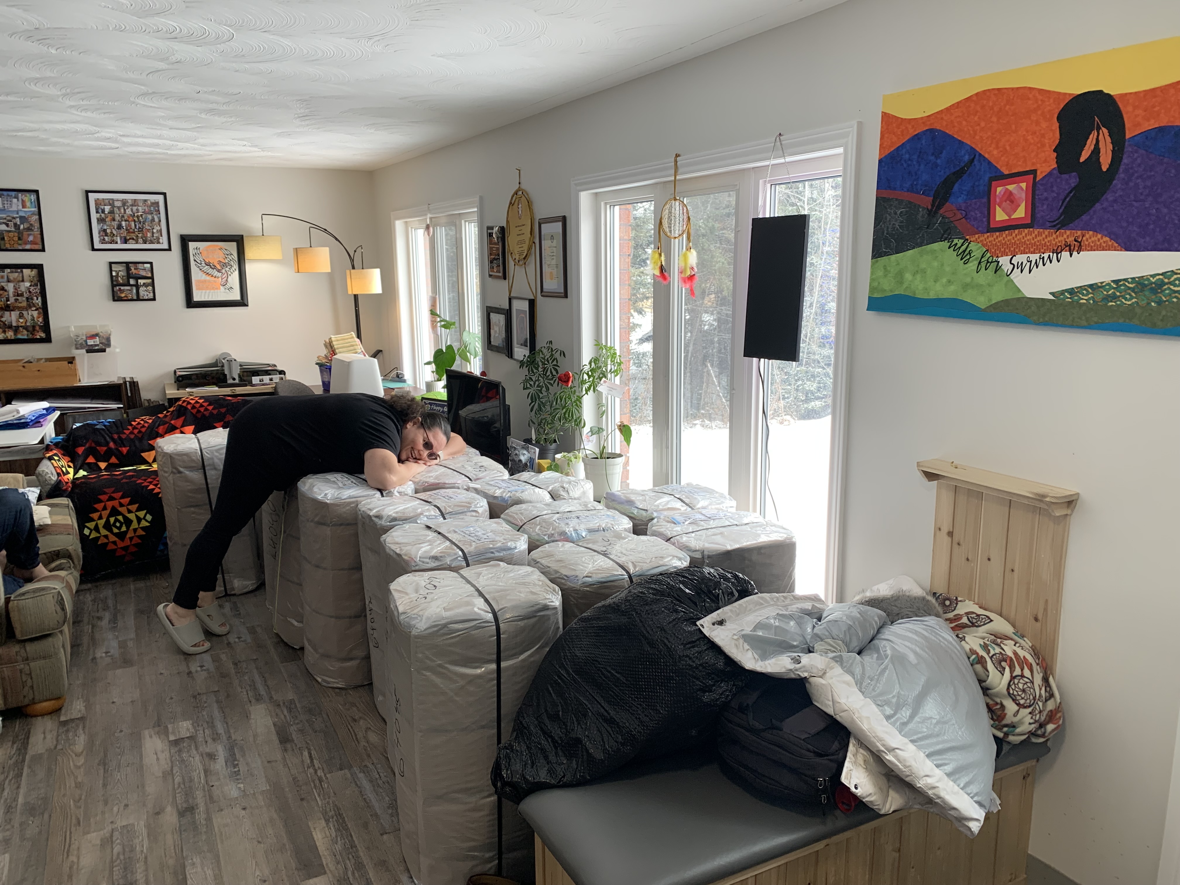 A woman in a living room hugs quilts that are prepared for shipping in white wrapping.