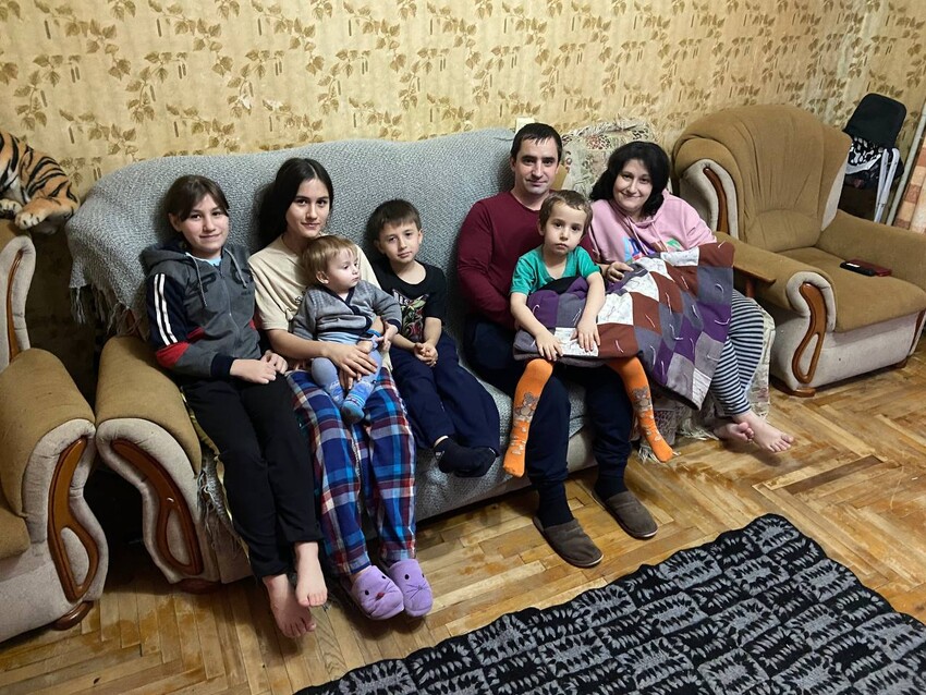 Julia (right), her husband and five children sit on a couch with an MCC comforter they received from MCC partner Zaporizhzhia Baptist Union. 