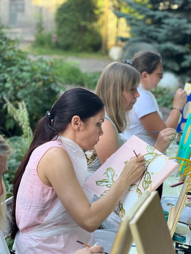 three women sitting in a row drawing on easels