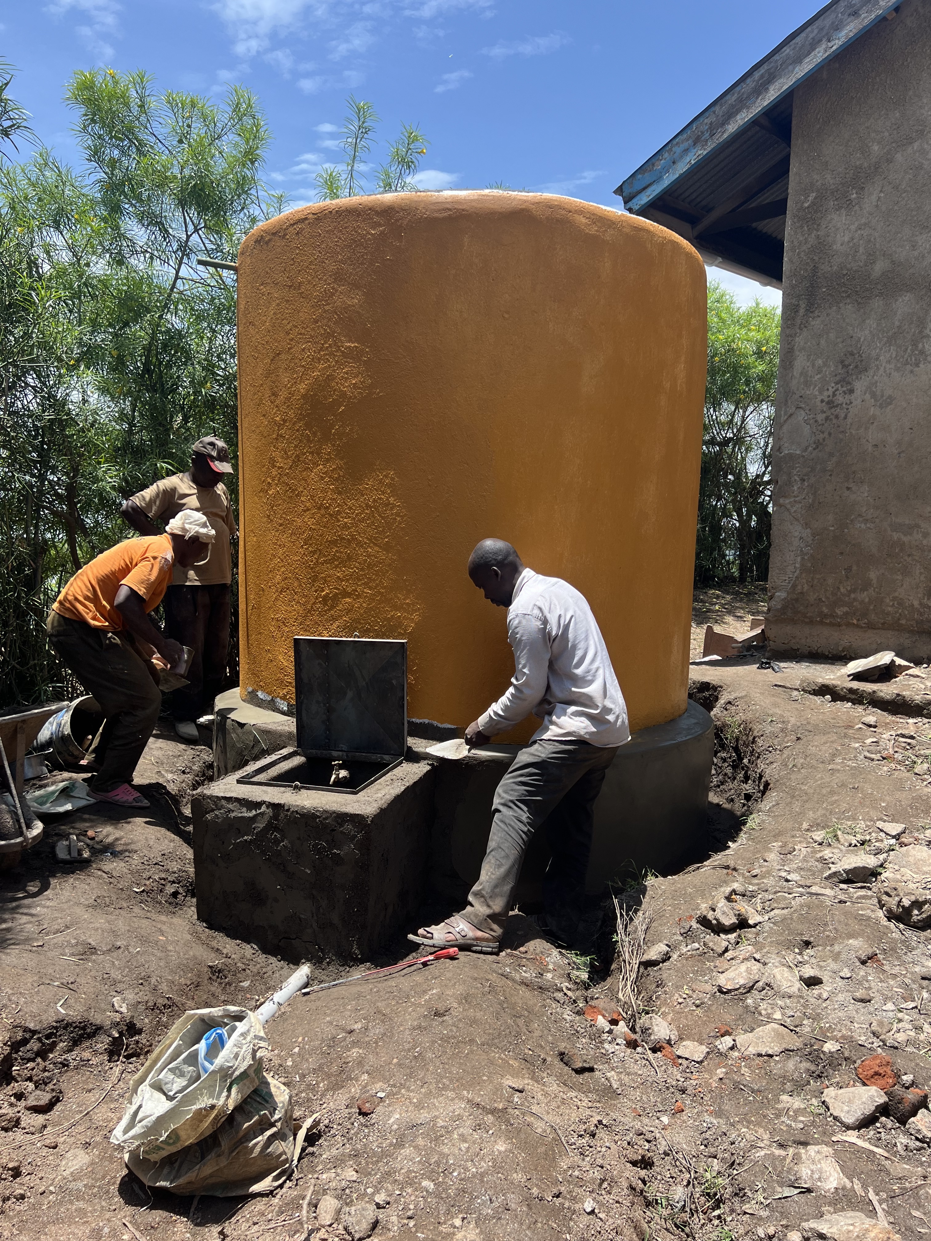 A rainwater harvesting tank that is under construction by Isingoma Yofesi (in front), Bwambale Uzia, left, and Kule Robert, right, at at Kithoma Primary School, Uganda.