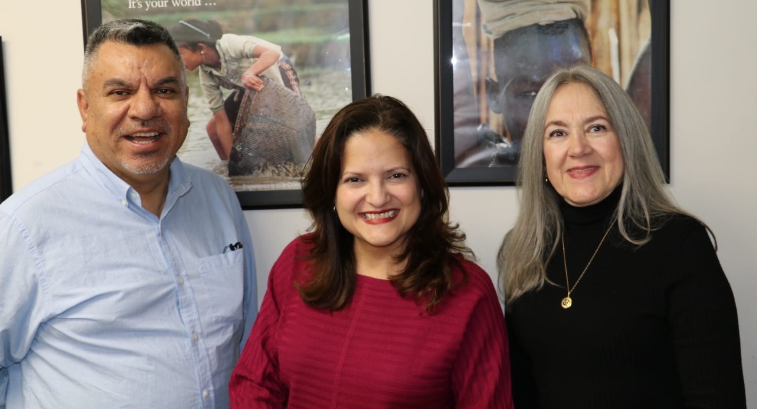 a man and two women posing for a group picture in front of pictures on the wall