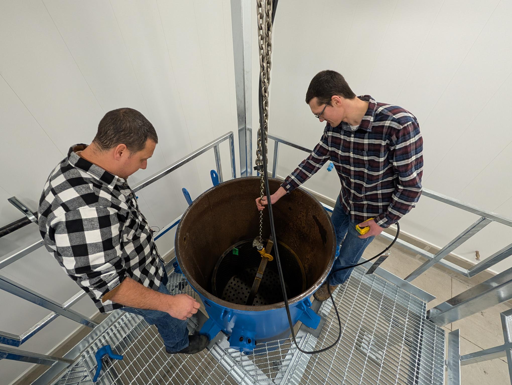 Two men look into a large round metal container. 