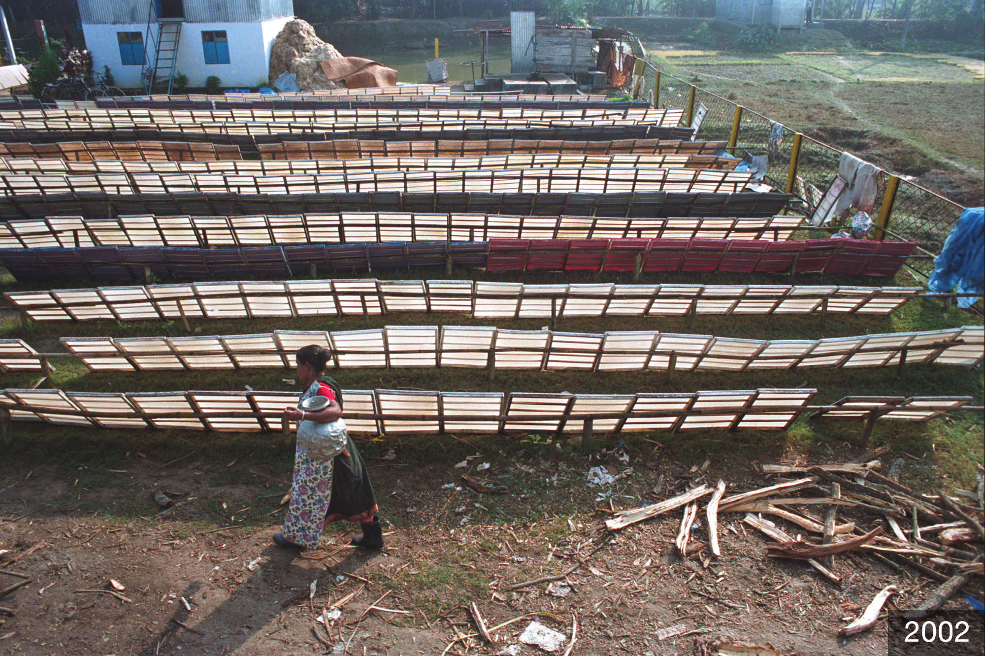A woman walks past rows of drying papers. The year 2002 is in the corner of the image.