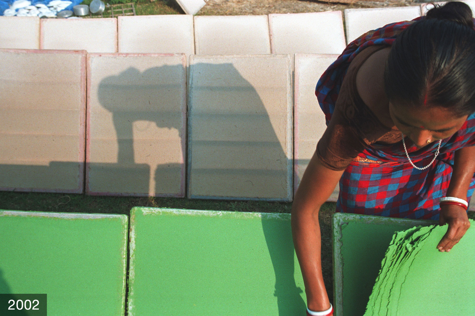 A woman removes green-dyed paper from an outdoor drying station.