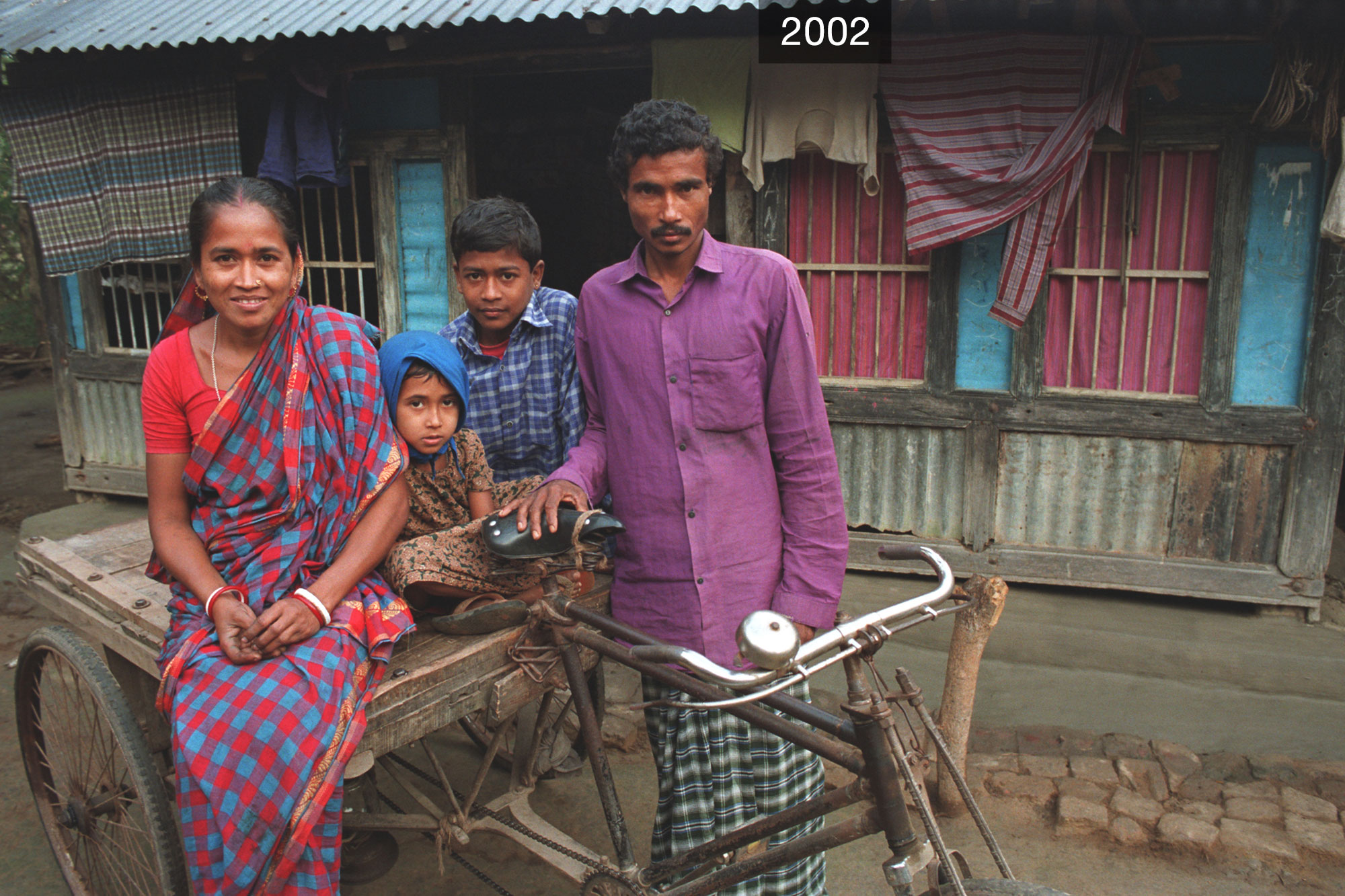 A family - two adults and two kids - sit pose on a 3-wheeled cycle.