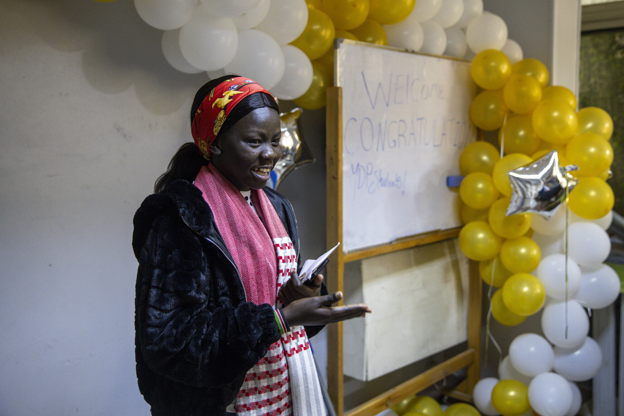 A person stands smiling near a whiteboard with welcoming text, surrounded by balloons and stars.