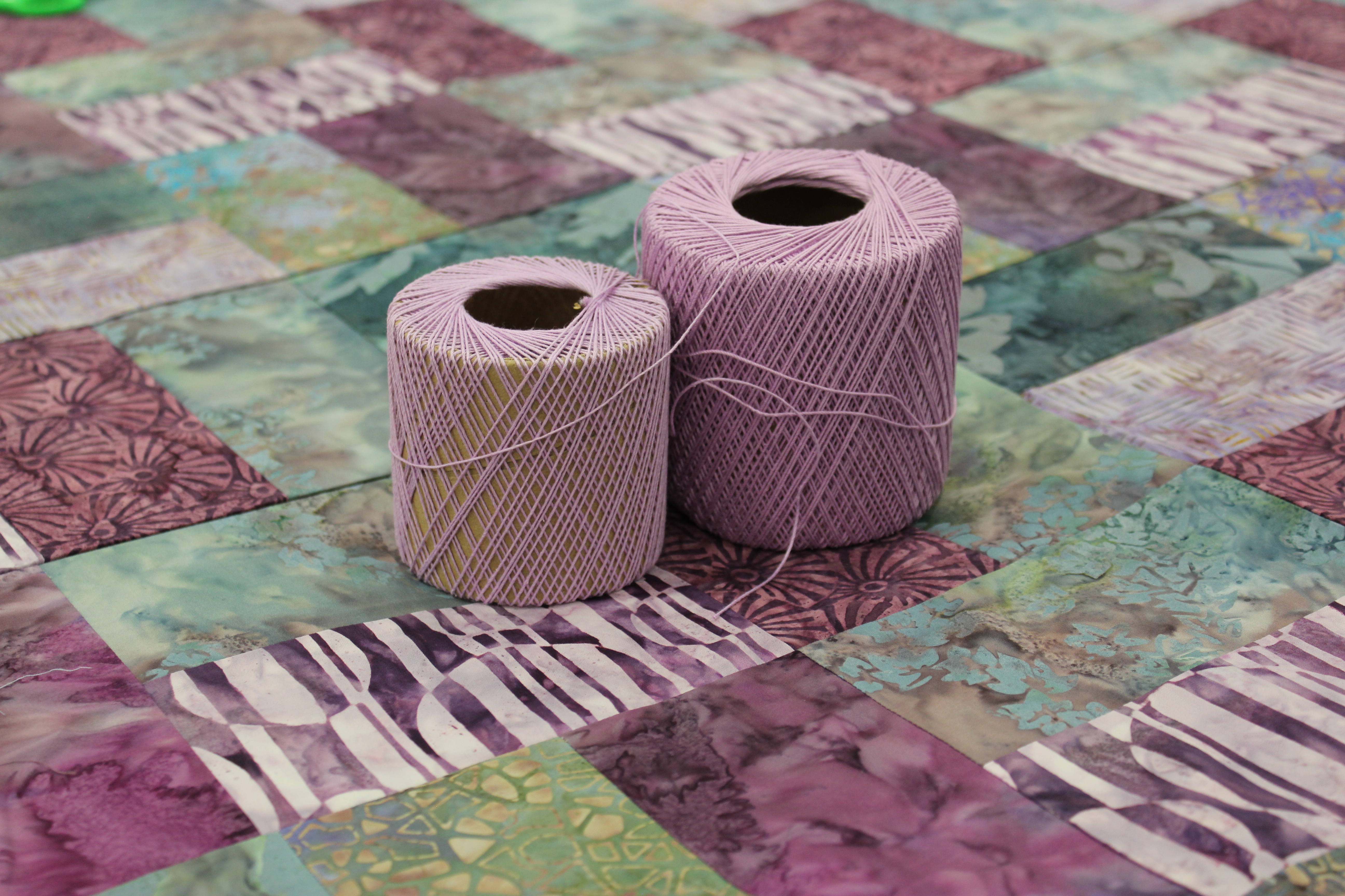 Two spools of thread sit on top of a quilt