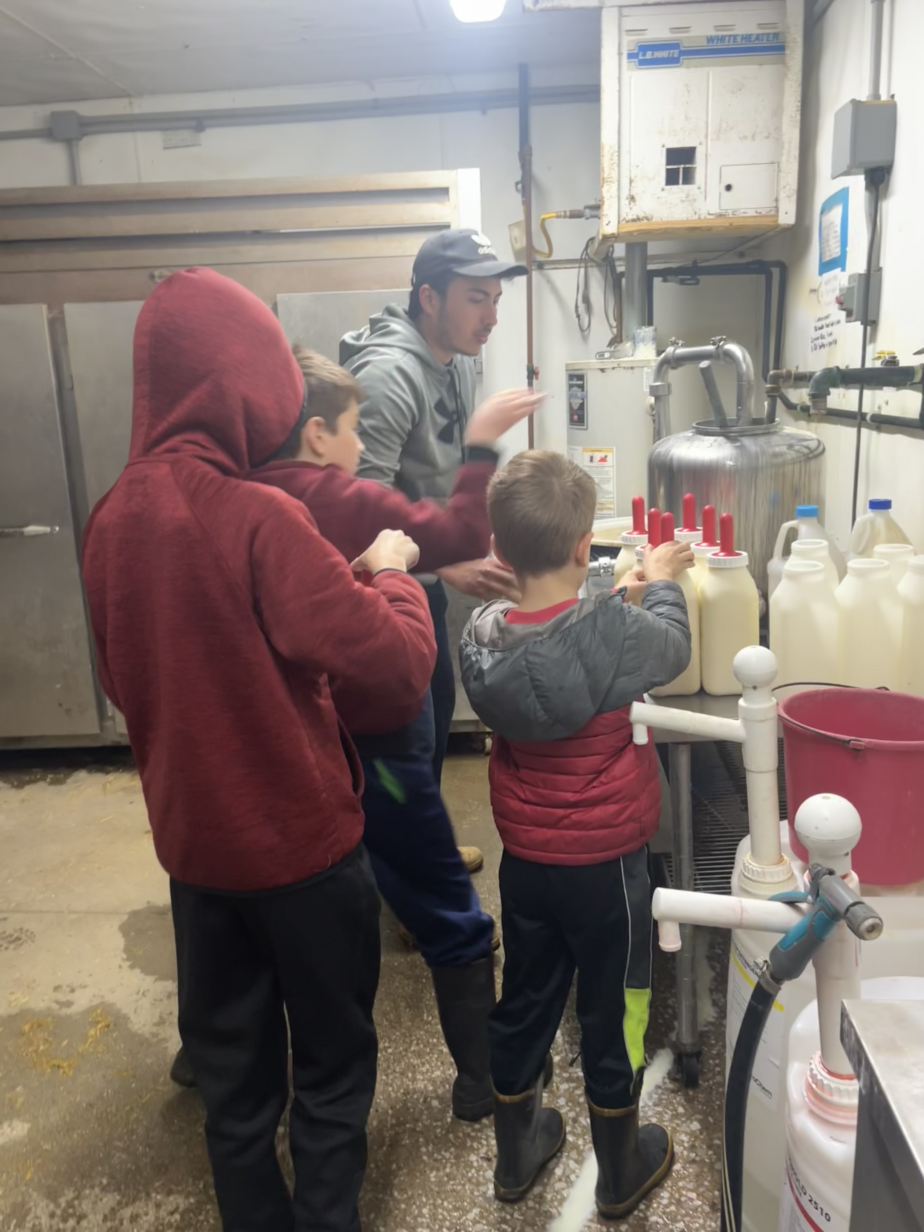 man and three boys stand around bottles of milk at a dairy farm