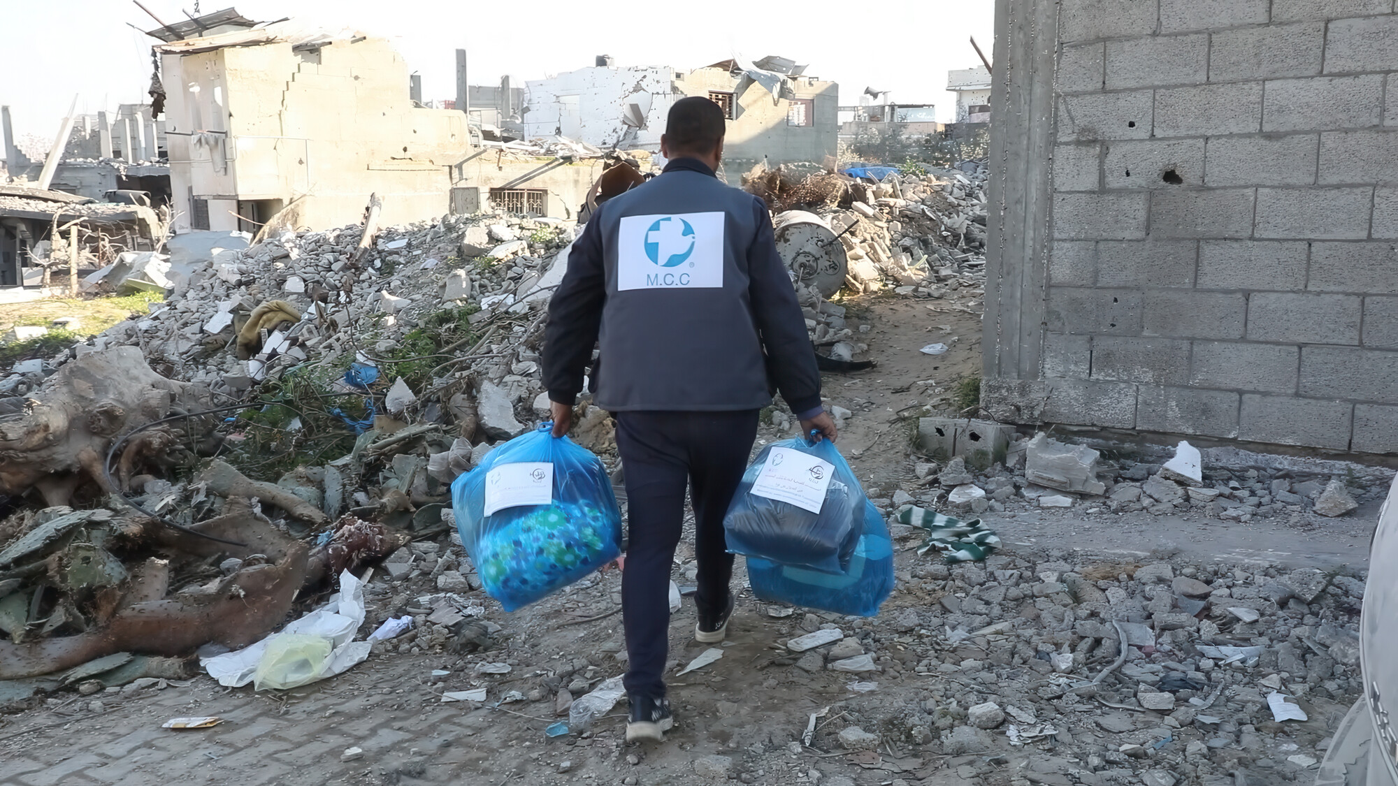 A man wearing a MCC vest carrying relief supplies through rubble in Gaza