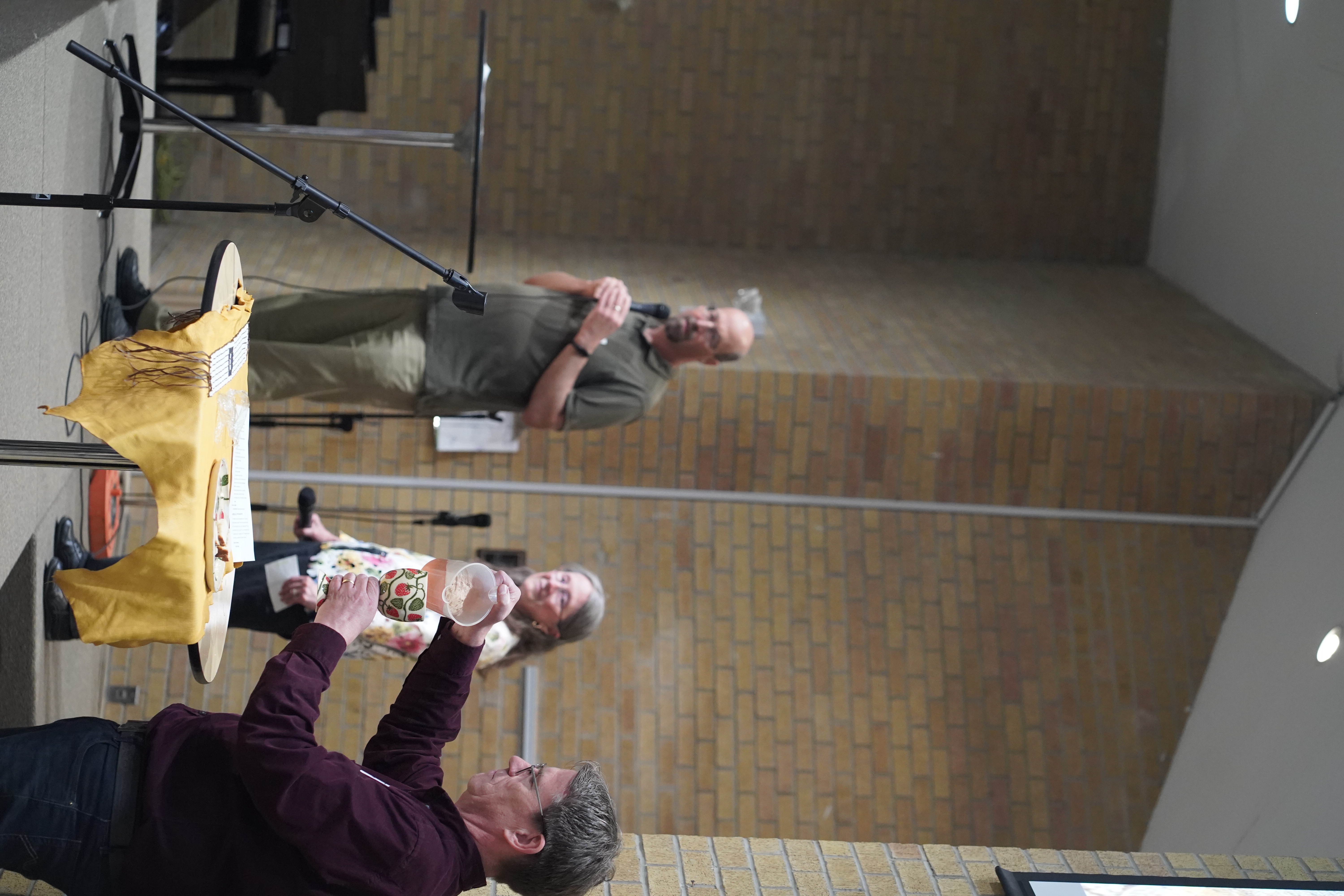 A man pours juice into a chalice while a man and woman in the background look on