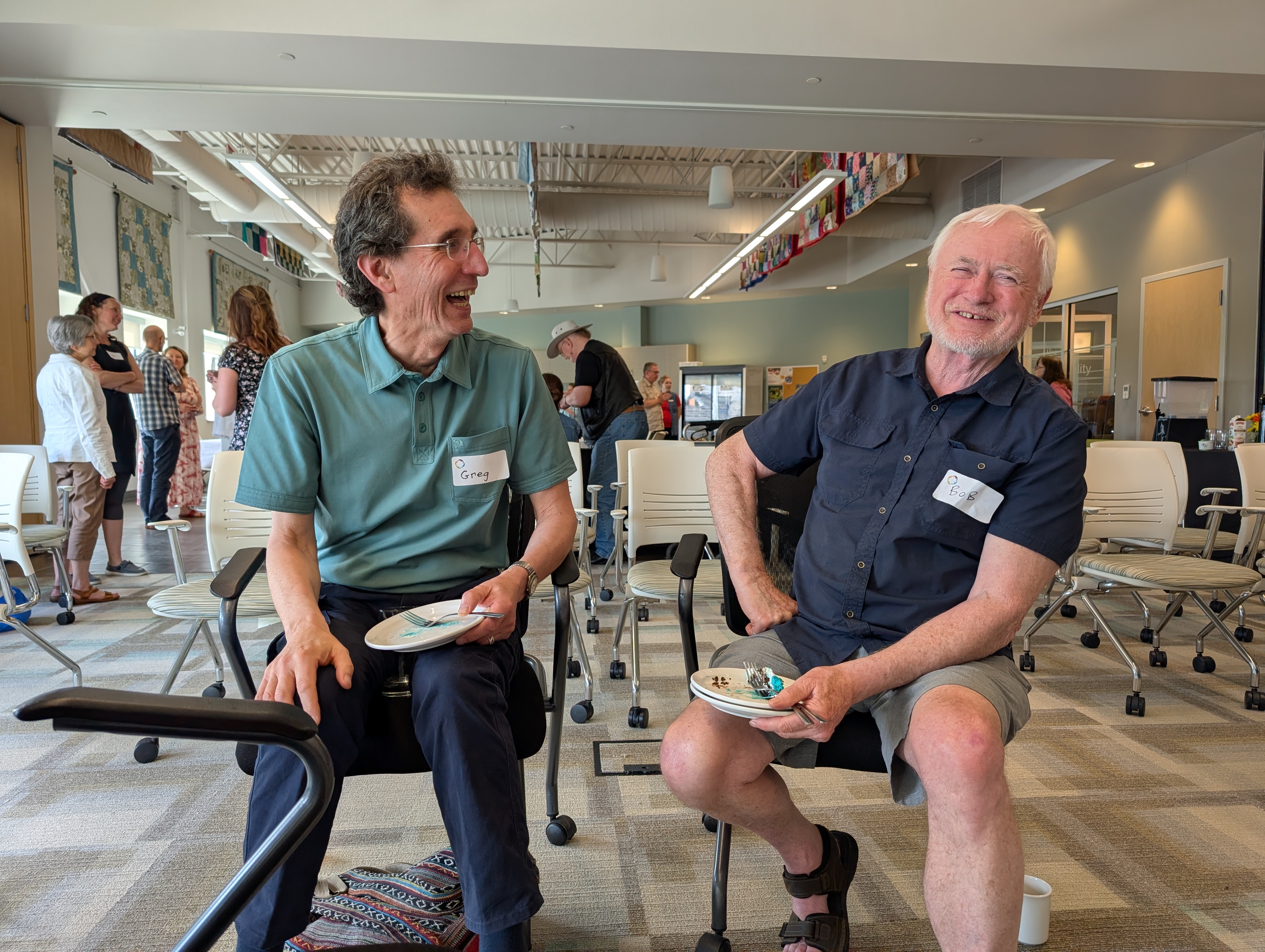 Two men sit beside each other laughing.