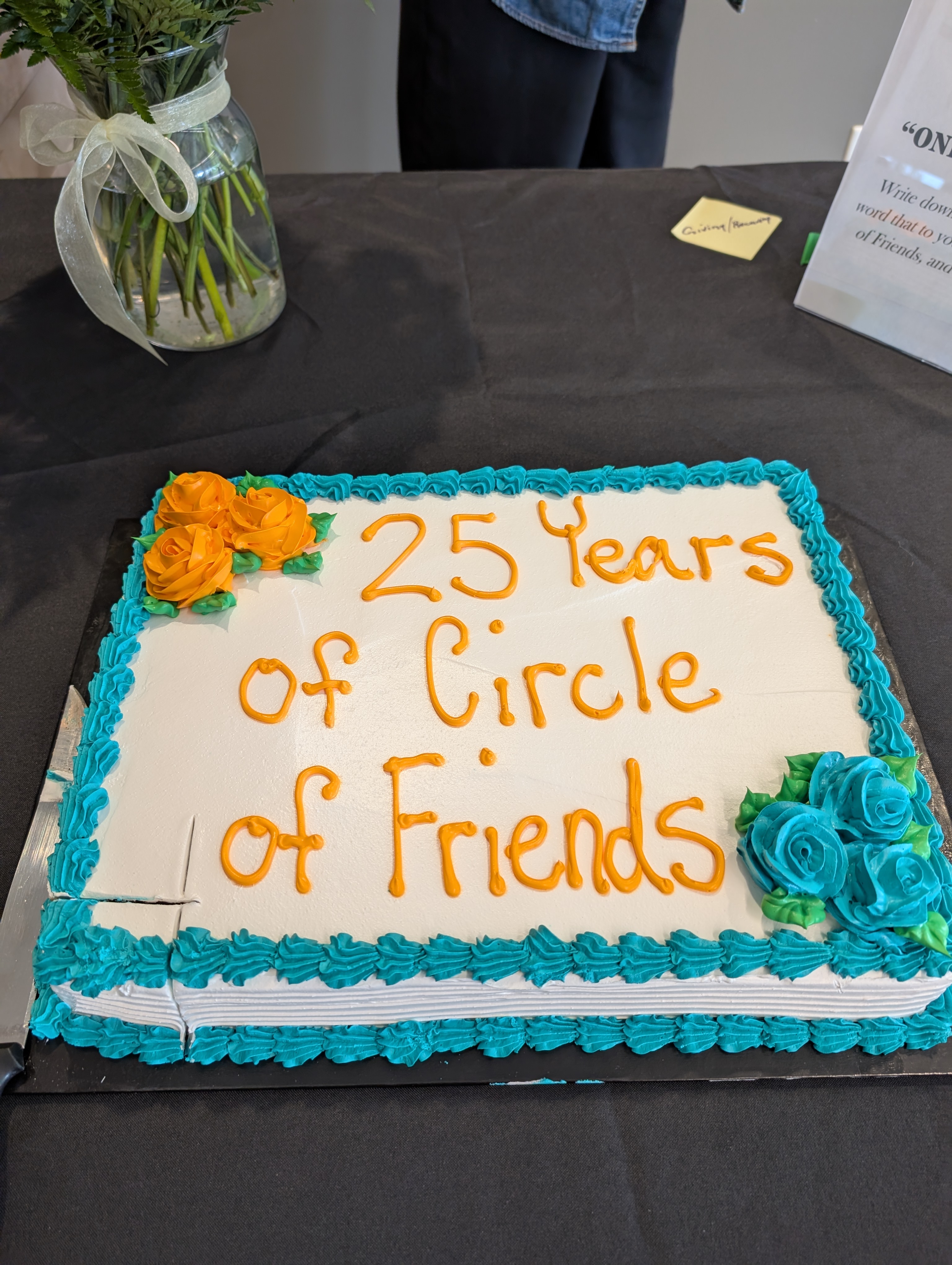 a white cake with blue frosting and orange writing that says "25 years of Circle of Friends"