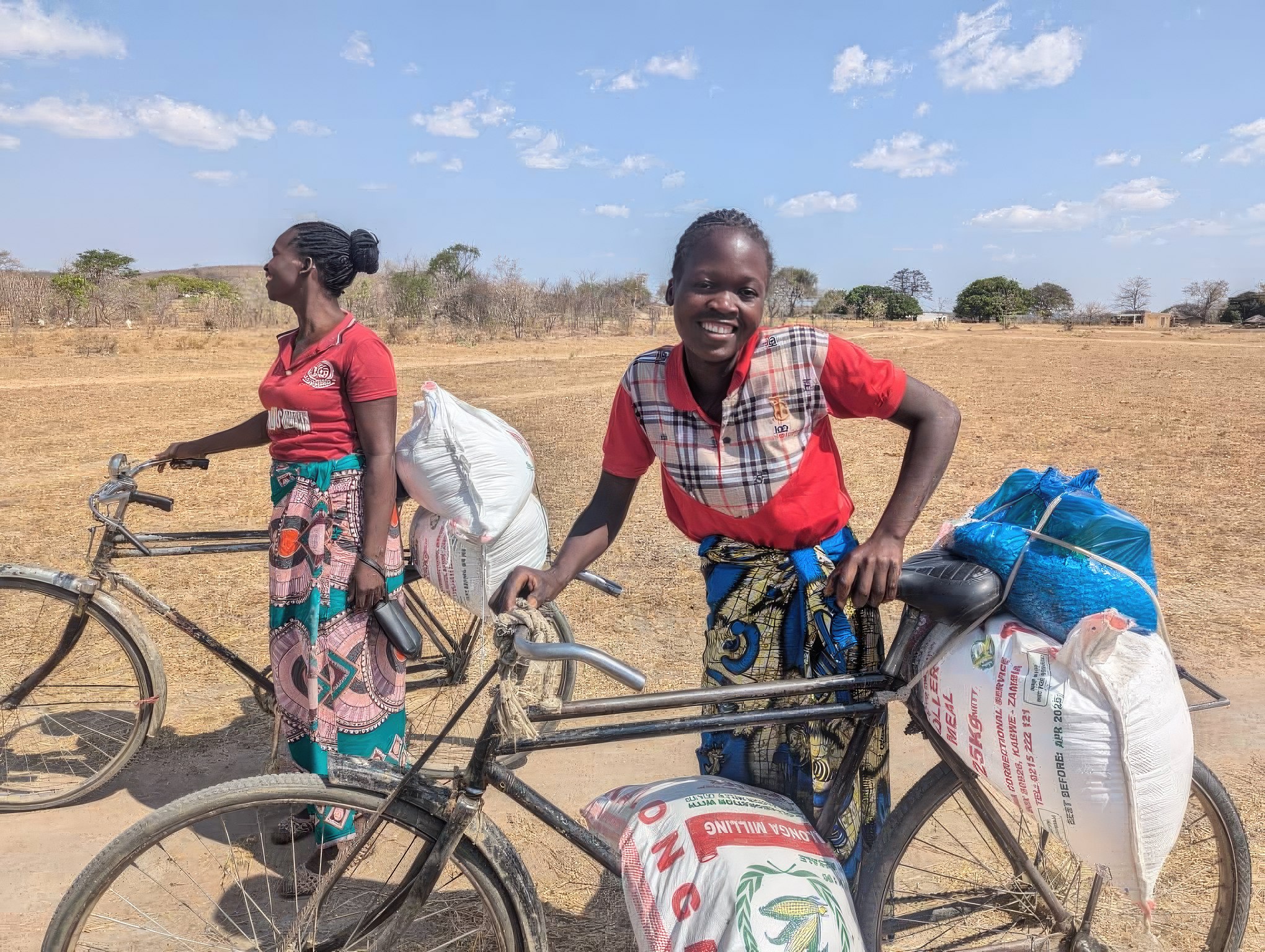 Chiloto Chizongo (right) and Juliet Chabokola (left) stand with their bikes loaded with bags of food provided to them from MCC partners.