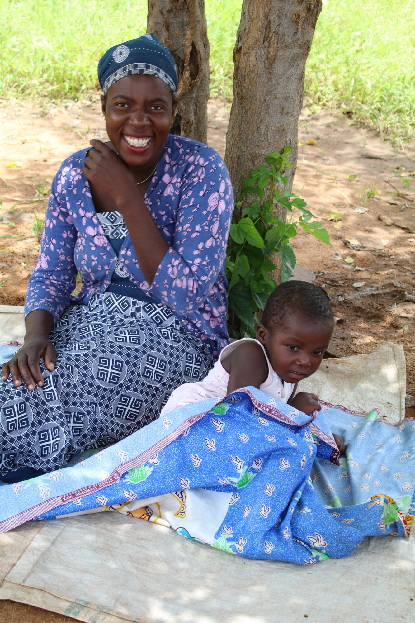 woman sitting under tree with child on blanket beside her