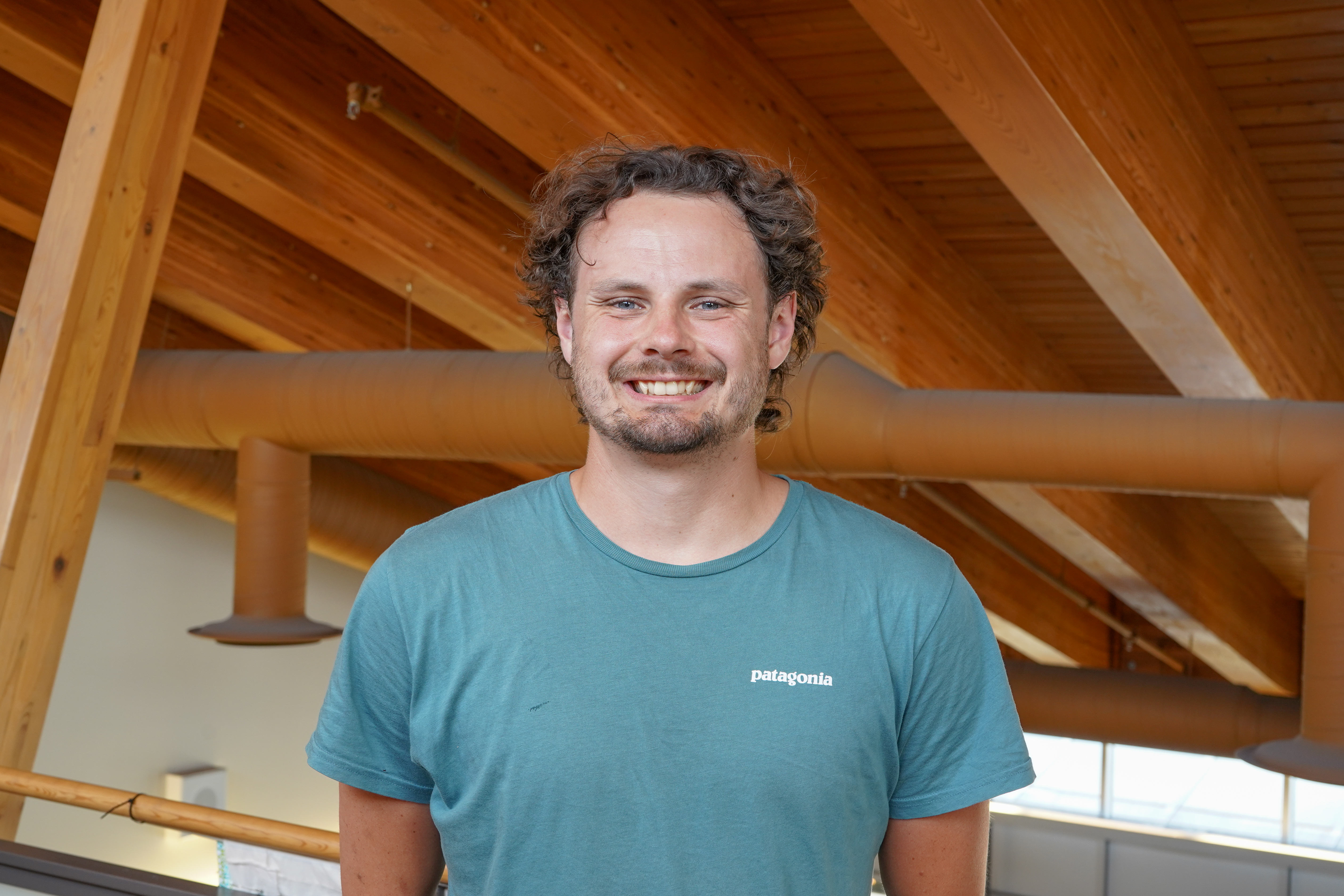Sasha smiles at the camera in front of a wooded background.