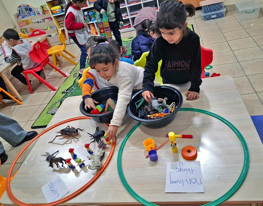 children kneel on floor to place small objects in two hulu hoops