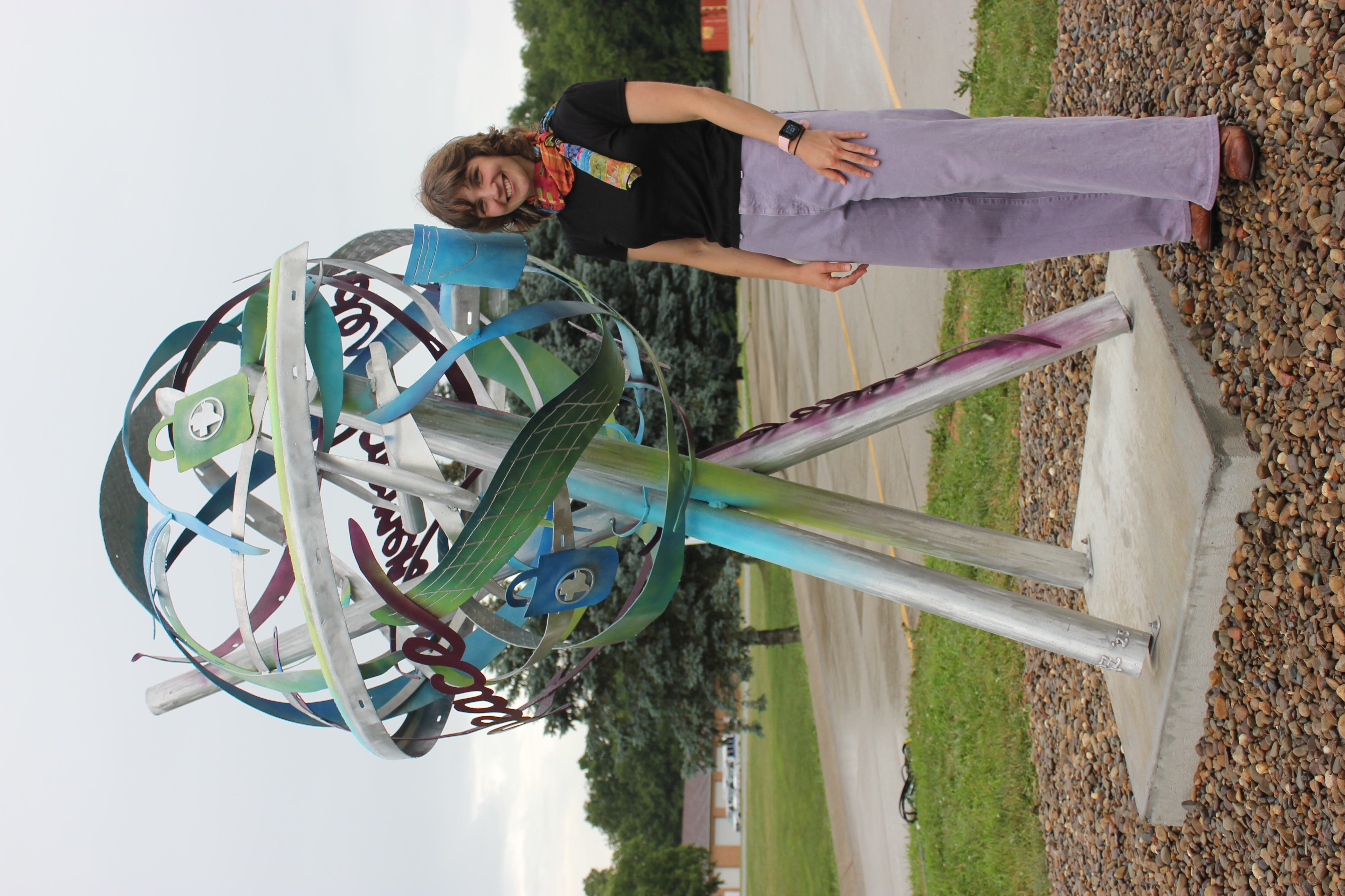 woman stands beside a large circular metal sculpture