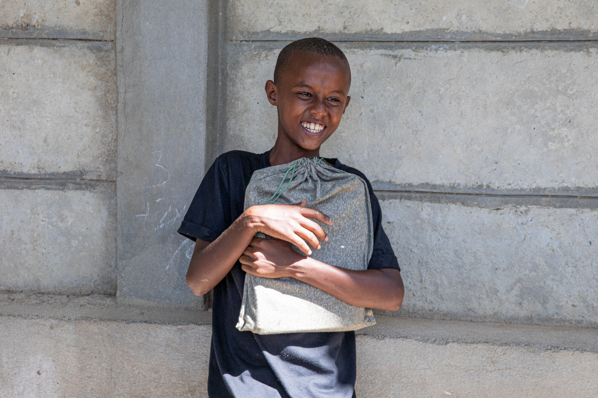 boy standing in front of cement wall holding package to his chest