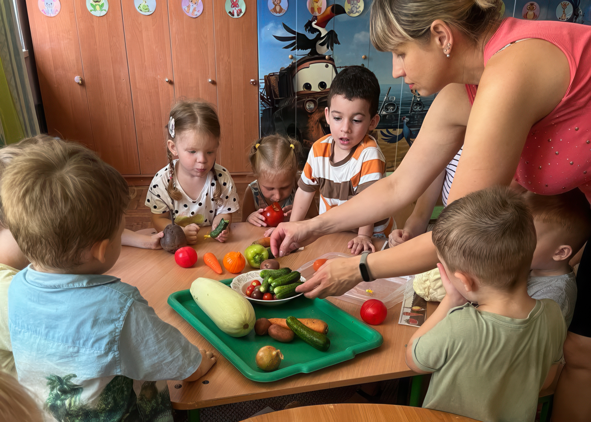 young children and teacher gathered around plate of pretend fruit and vegetables