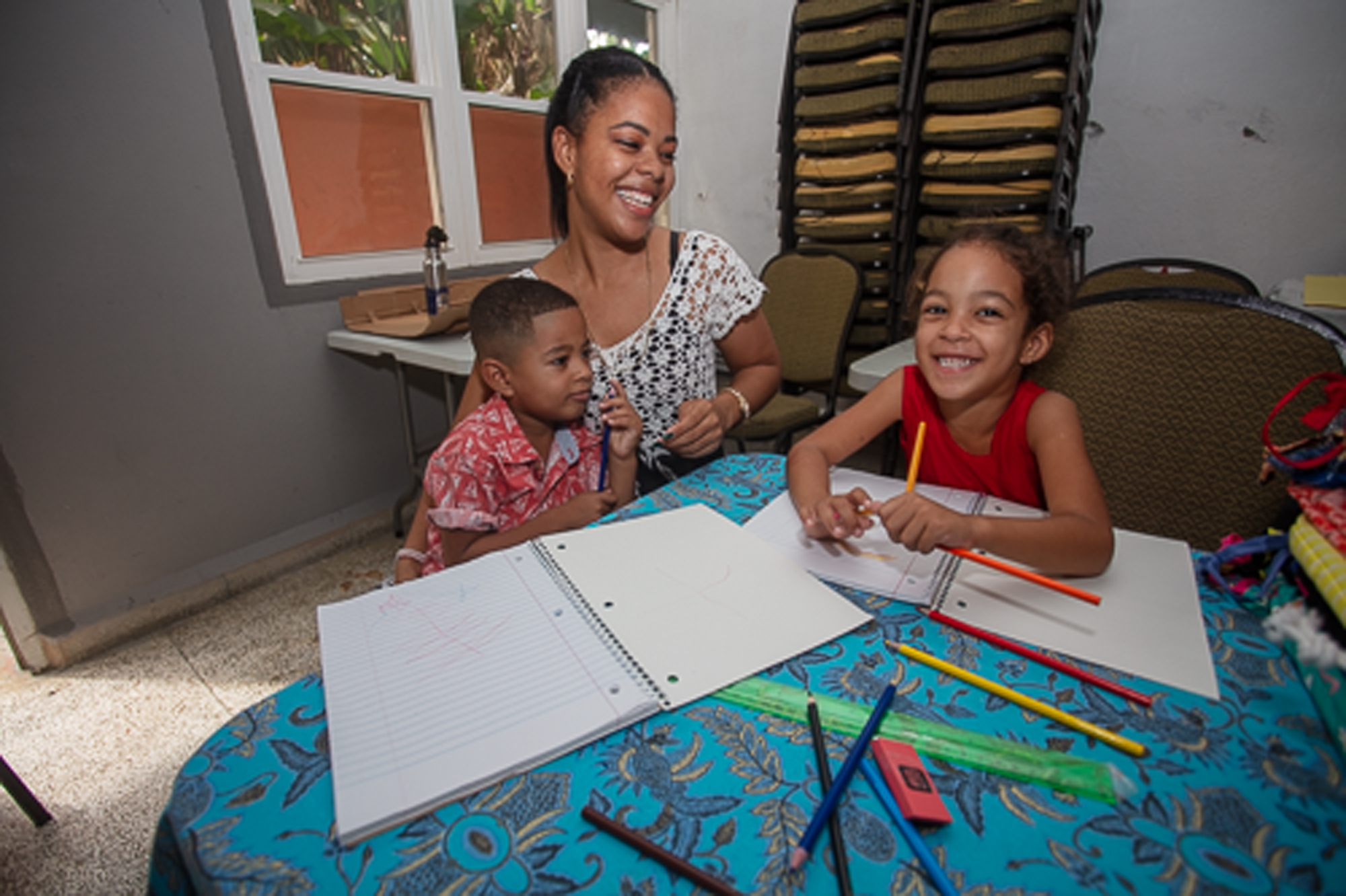 mother and two children, holding colored pencils, sit at the table with open notebooks