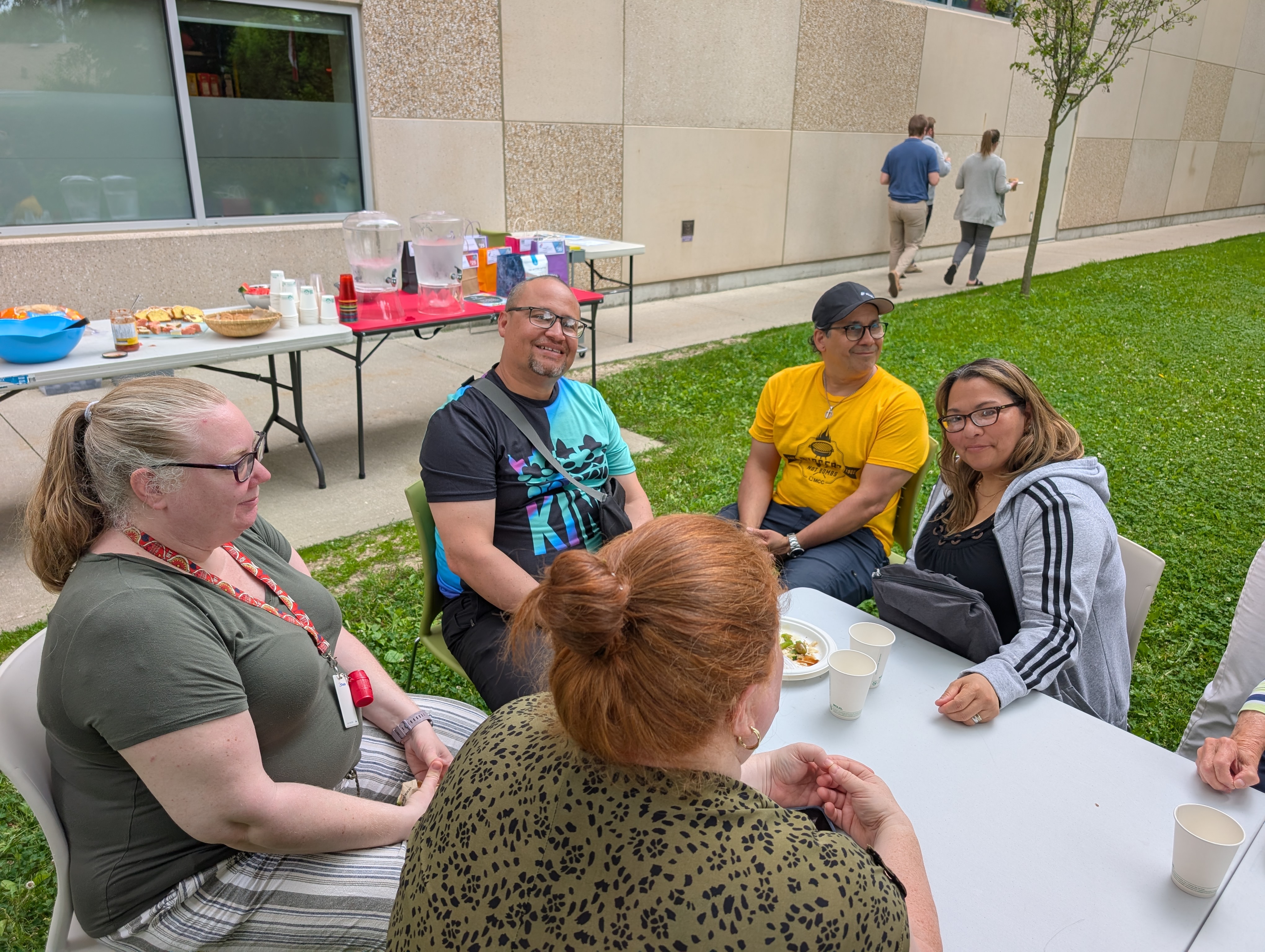 Members of the Salazar family and MCC sit around a table outdoors at a BBQ event.