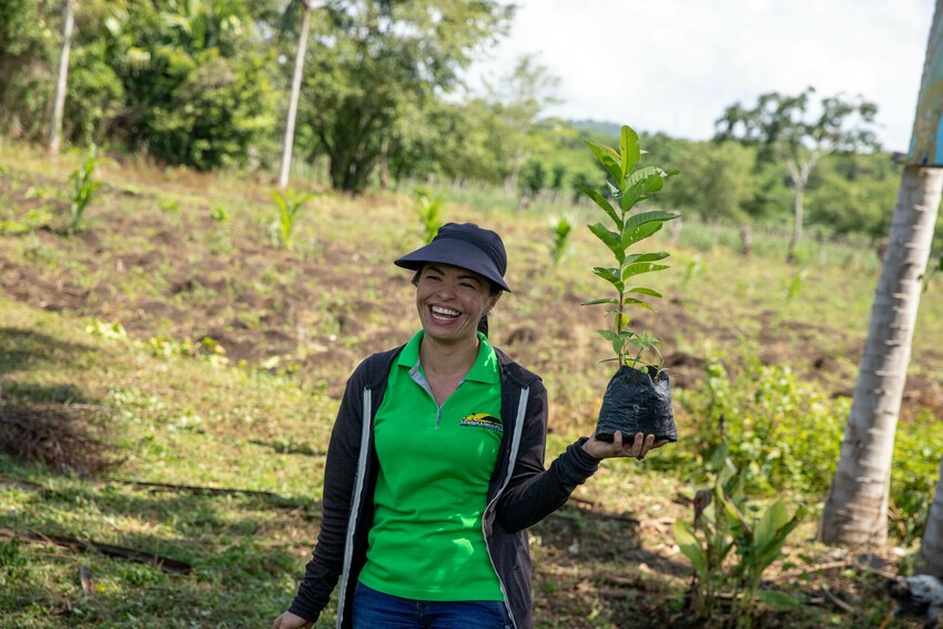 A woman smiling holding up a tree seedling