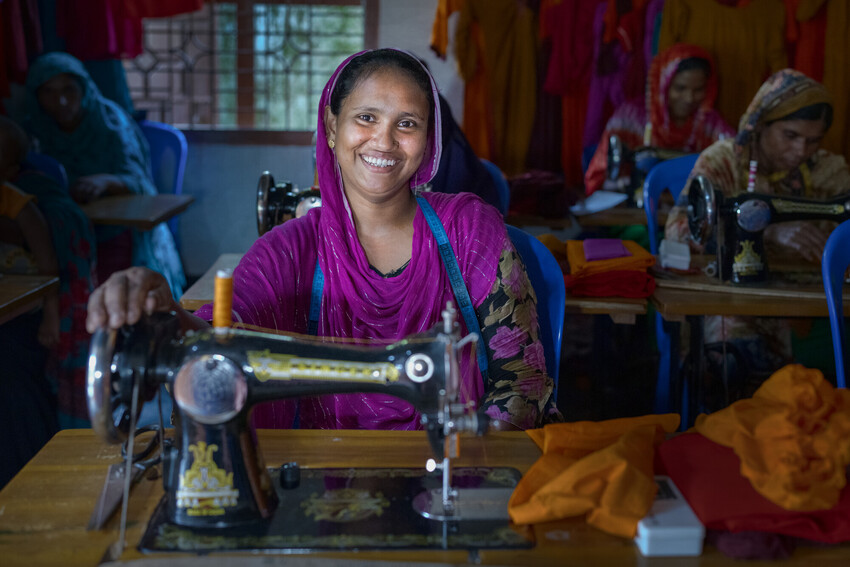 A woman smiling sitting at a sewing machine