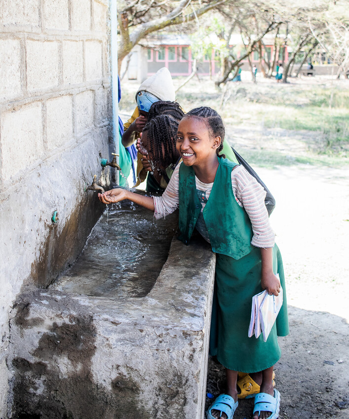 Young children drinking from a faucet at a school