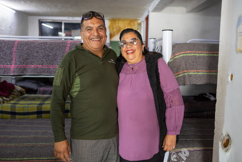 A man and woman smiling for a photo in front of a room of bunk beds