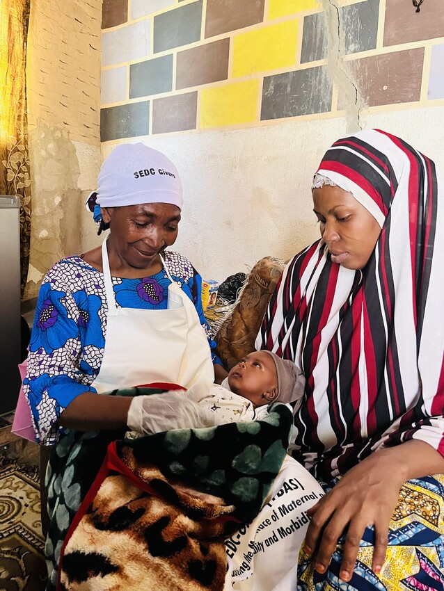 A mother holds her young baby with a doctor sitting next to them performing a check up