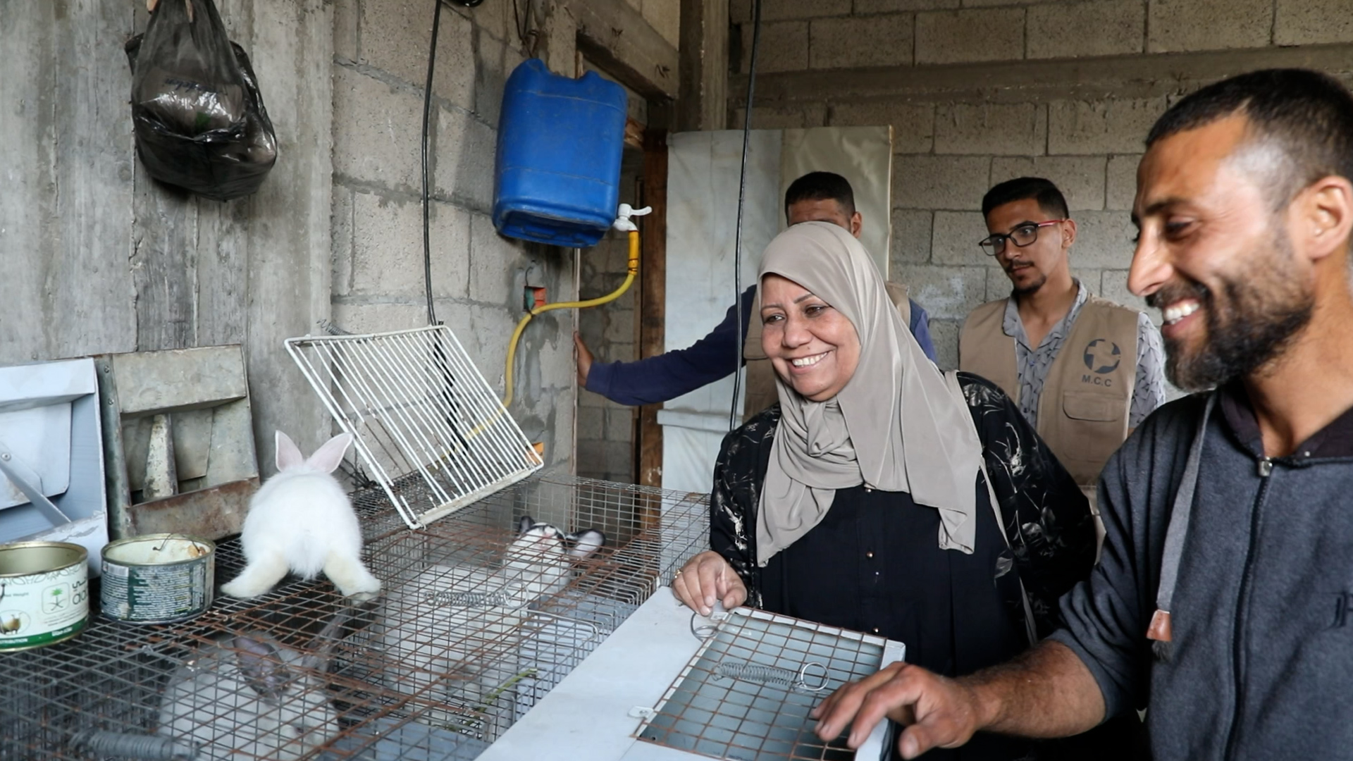 woman and man smiling while looking at rabbit on top of cage