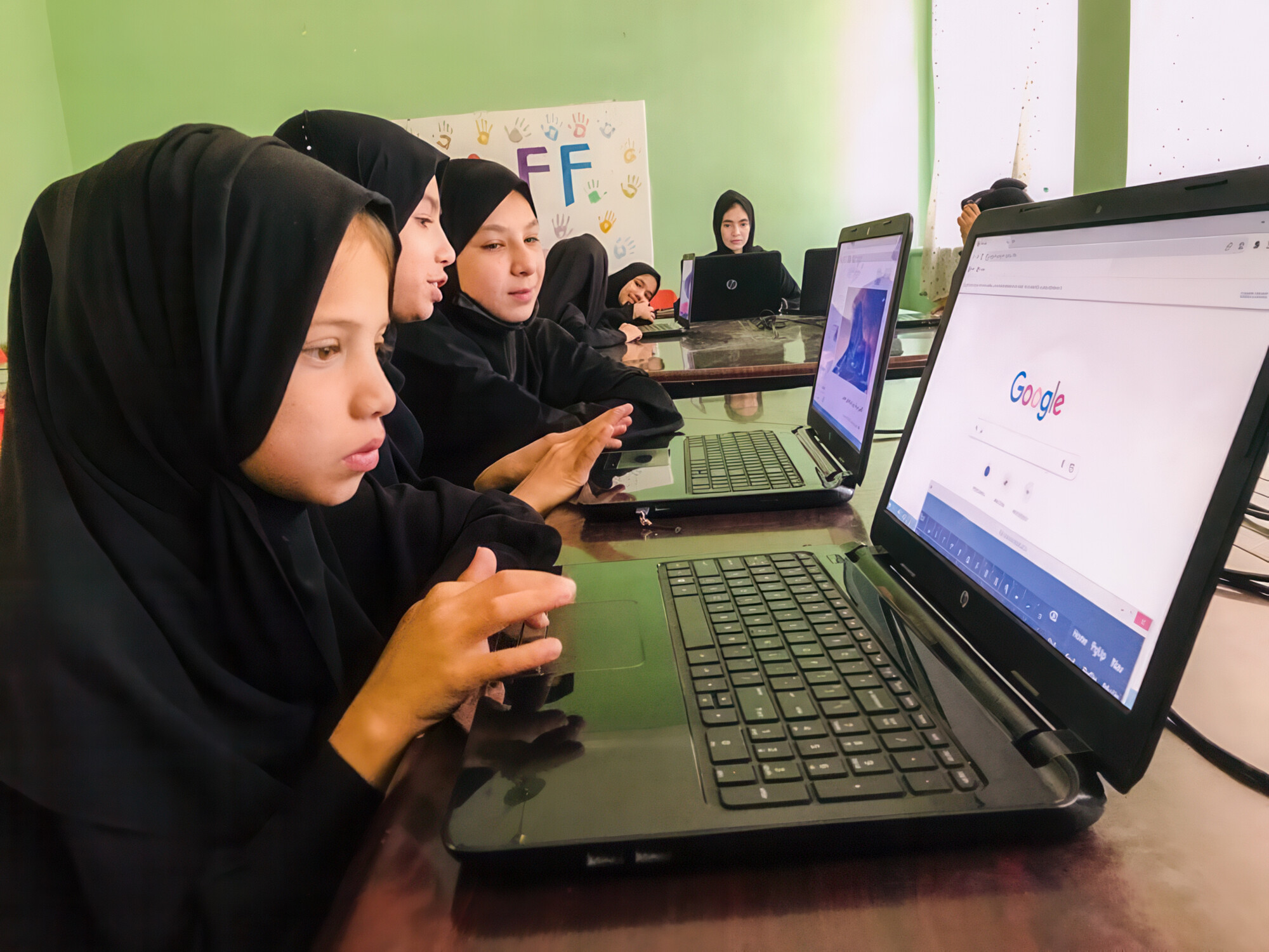 girls wearing black clothes and head coverings work on the computer