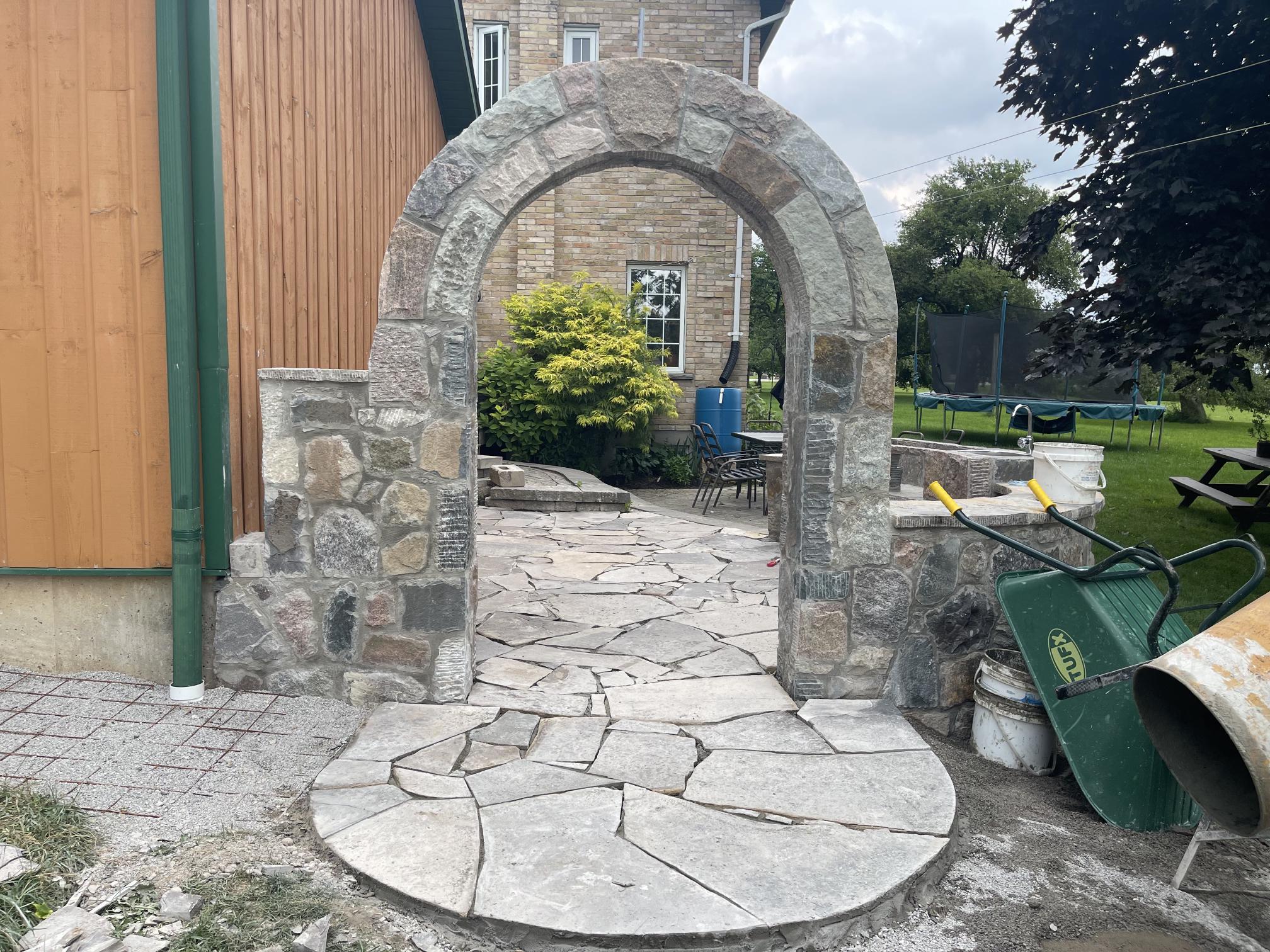 A stone archway over a stone patio on the side of a farmhouse