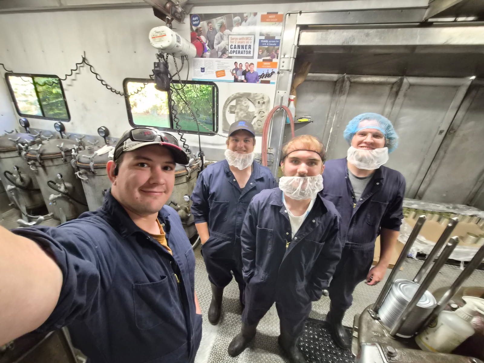 four men standing in a row pose for selfie with metal equipment in the background
