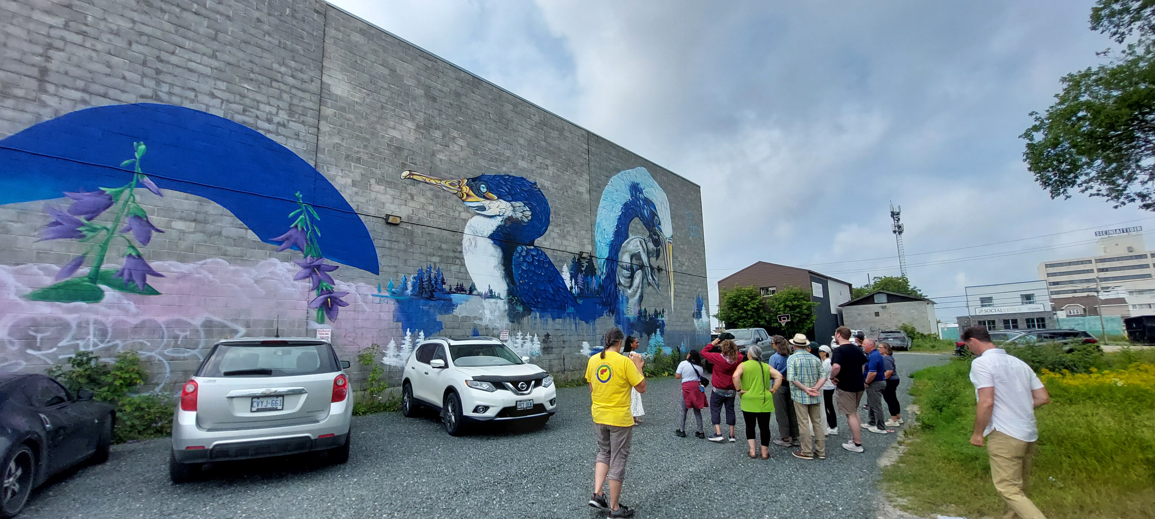 People gather to look at a grey stone wall with an Indigenous mural on it.