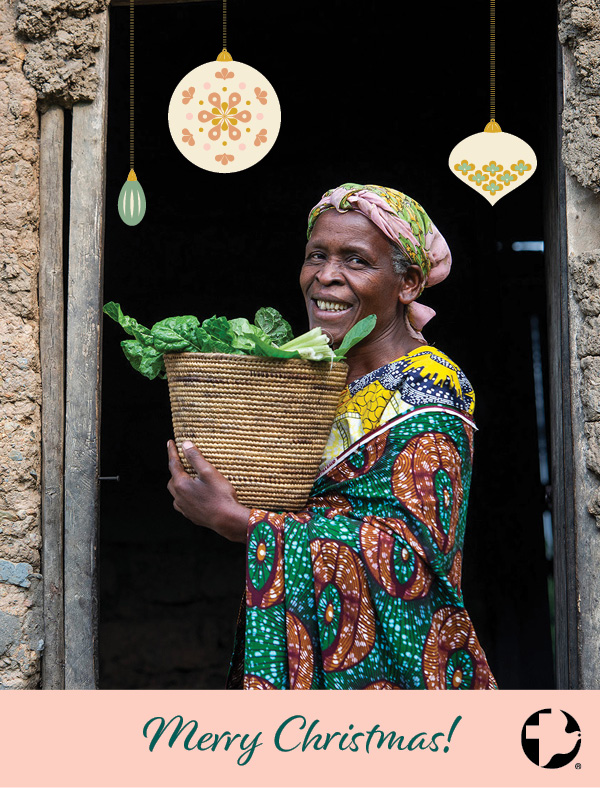 The front of an MCC Christmas card that features a woman smiling holding a basket of green vegetables.
